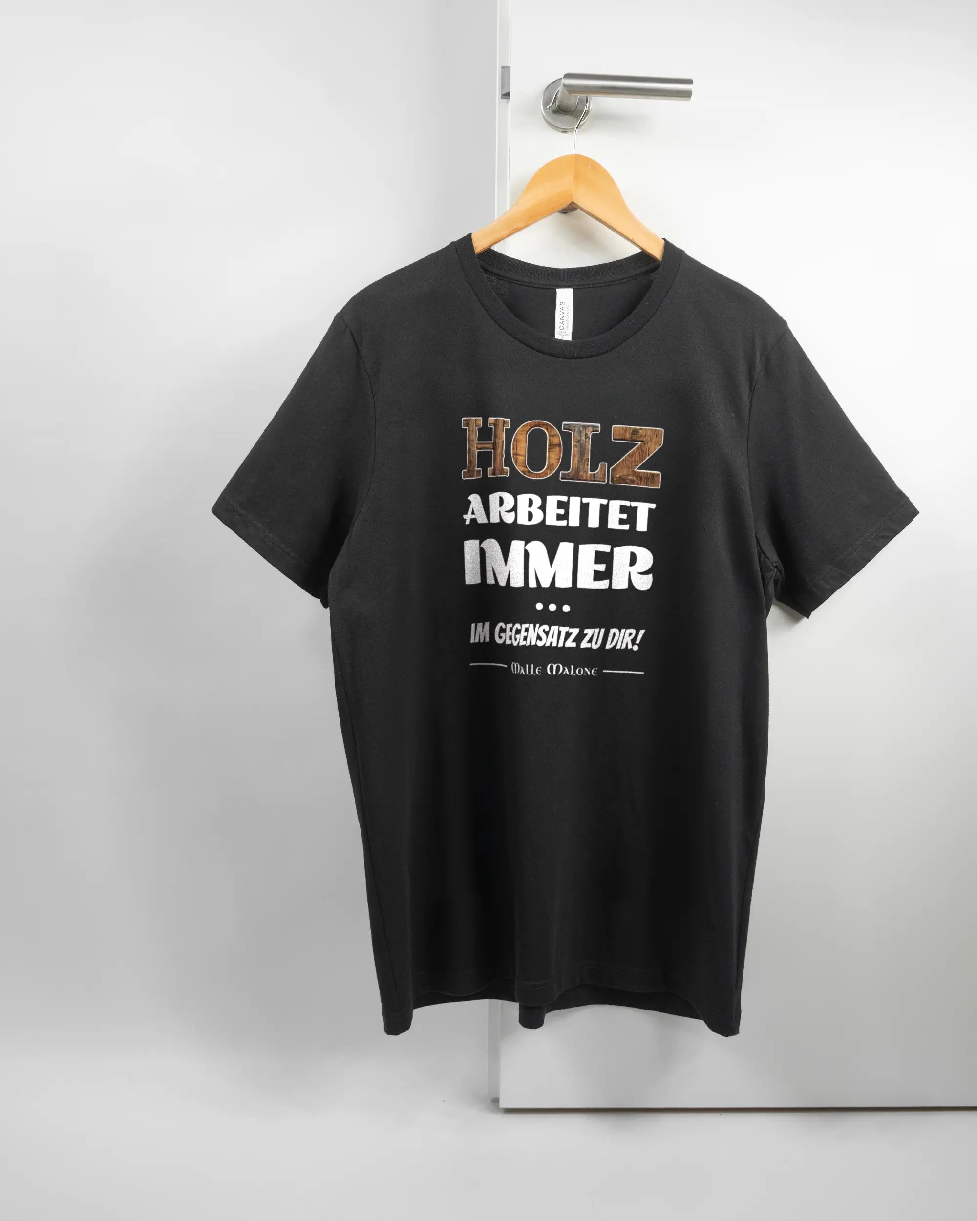 Vorderseite des Basic Unisex T-Shirt Light von Maondo mit dem Design Holzarbeit in der Farbe Black und in der Größe L auf einem Bügel an der Türklinke aufgehängt