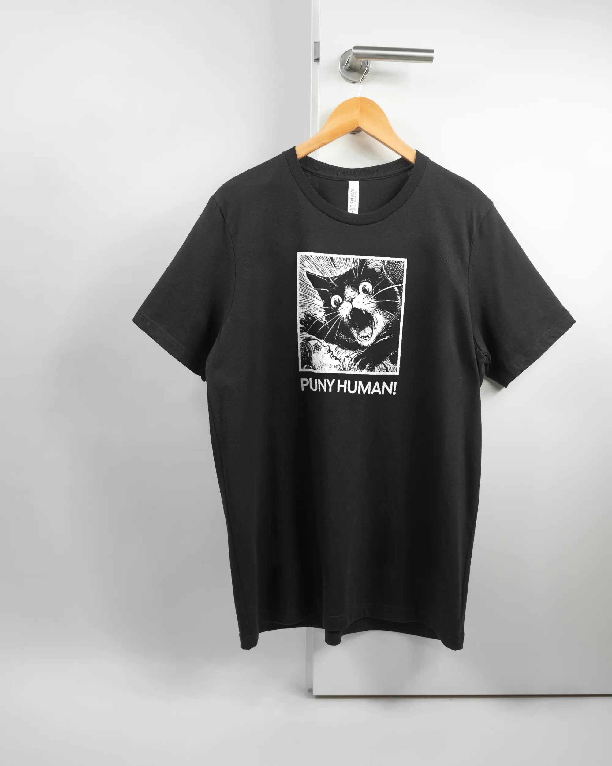 Vorderseite des Basic Unisex T-Shirt Light von Maondo mit dem Design Puny Human in der Farbe Black und in der Größe L auf einem Bügel an der Türklinke aufgehängt
