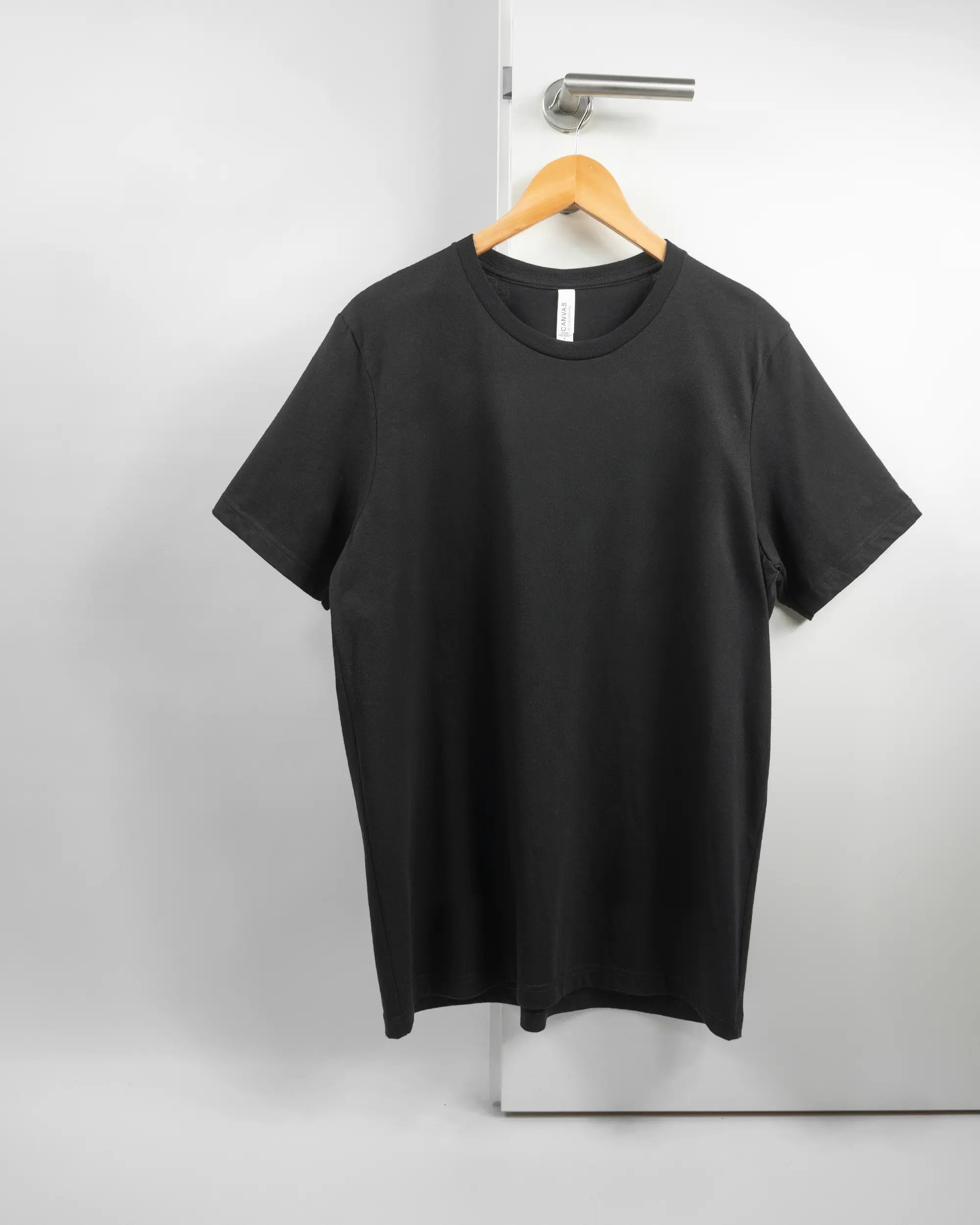 Vorderseite des Basic Unisex T-Shirt Light von Maondo ohne Motiv in der Farbe Black und in der Größe L auf einem Bügel an der Türklinke aufgehängt