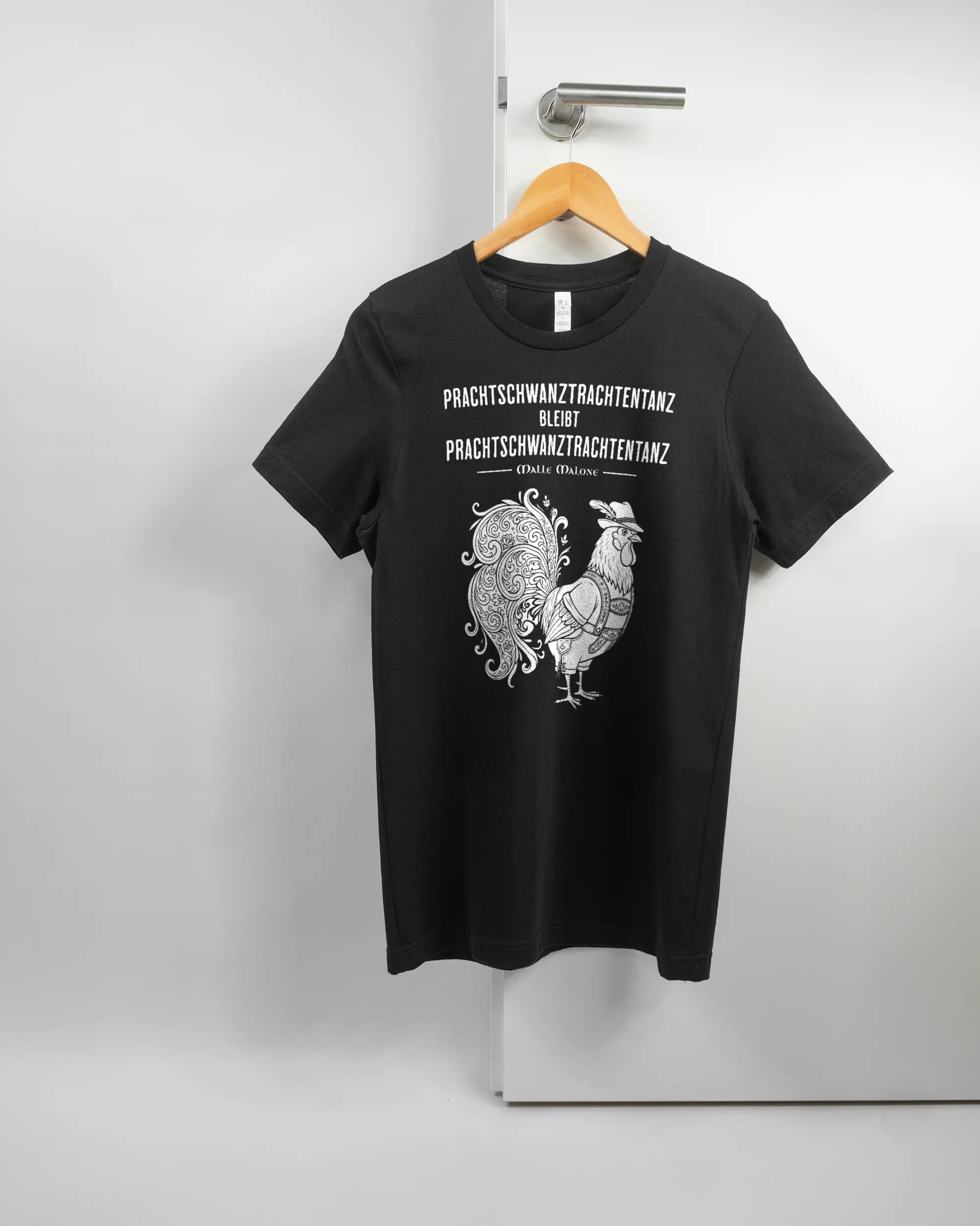 Vorderseite des Basic Unisex T-Shirt Light von Maondo mit dem Design Trachtentanz in der Farbe Black und in der Größe S auf einem Bügel an der Türklinke aufgehängt