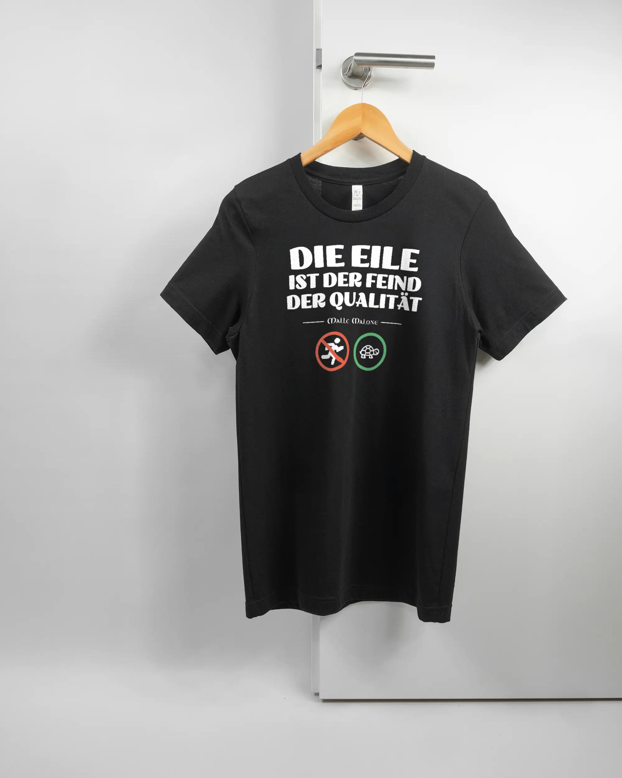 Vorderseite des Basic Unisex T-Shirt Light von Maondo mit dem Design Keine Eile in der Farbe Black und in der Größe S auf einem Bügel an der Türklinke aufgehängt