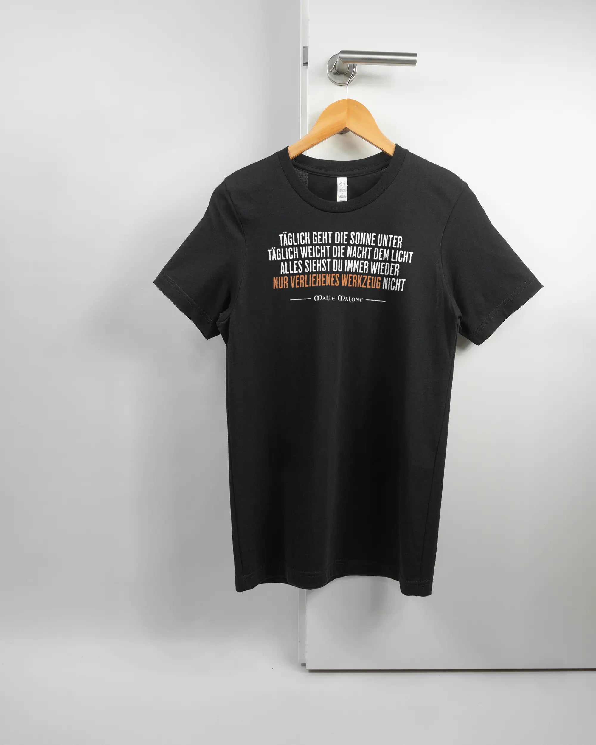 Vorderseite des Basic Unisex T-Shirt Light von Maondo mit dem Design Wegzeug in der Farbe Black und in der Größe S auf einem Bügel an der Türklinke aufgehängt