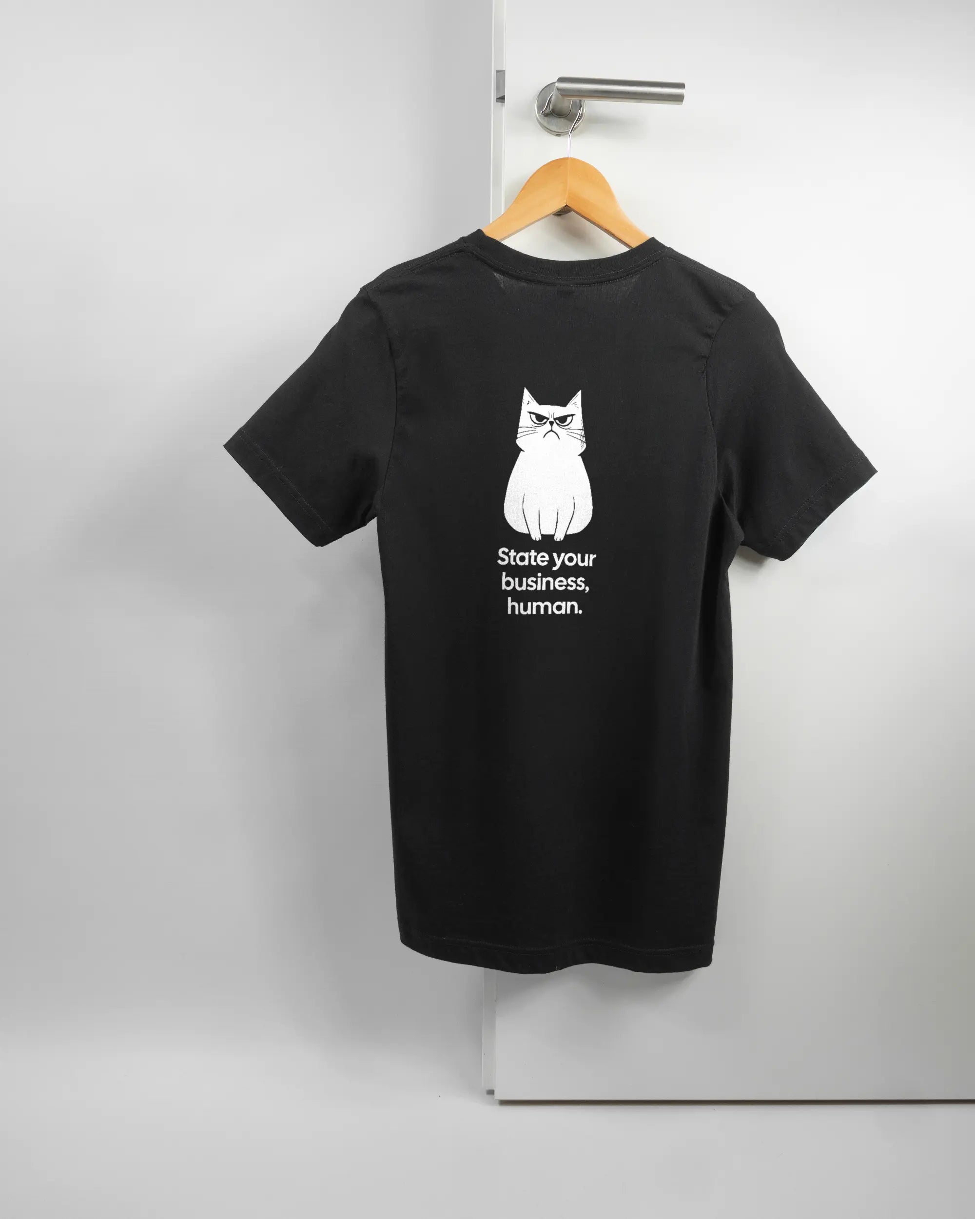 Rückseite des Basic Unisex T-Shirt Light von Maondo mit dem Design Grumpy Purr in der Farbe Black und in der Größe S auf einem Bügel an der Türklinke aufgehängt