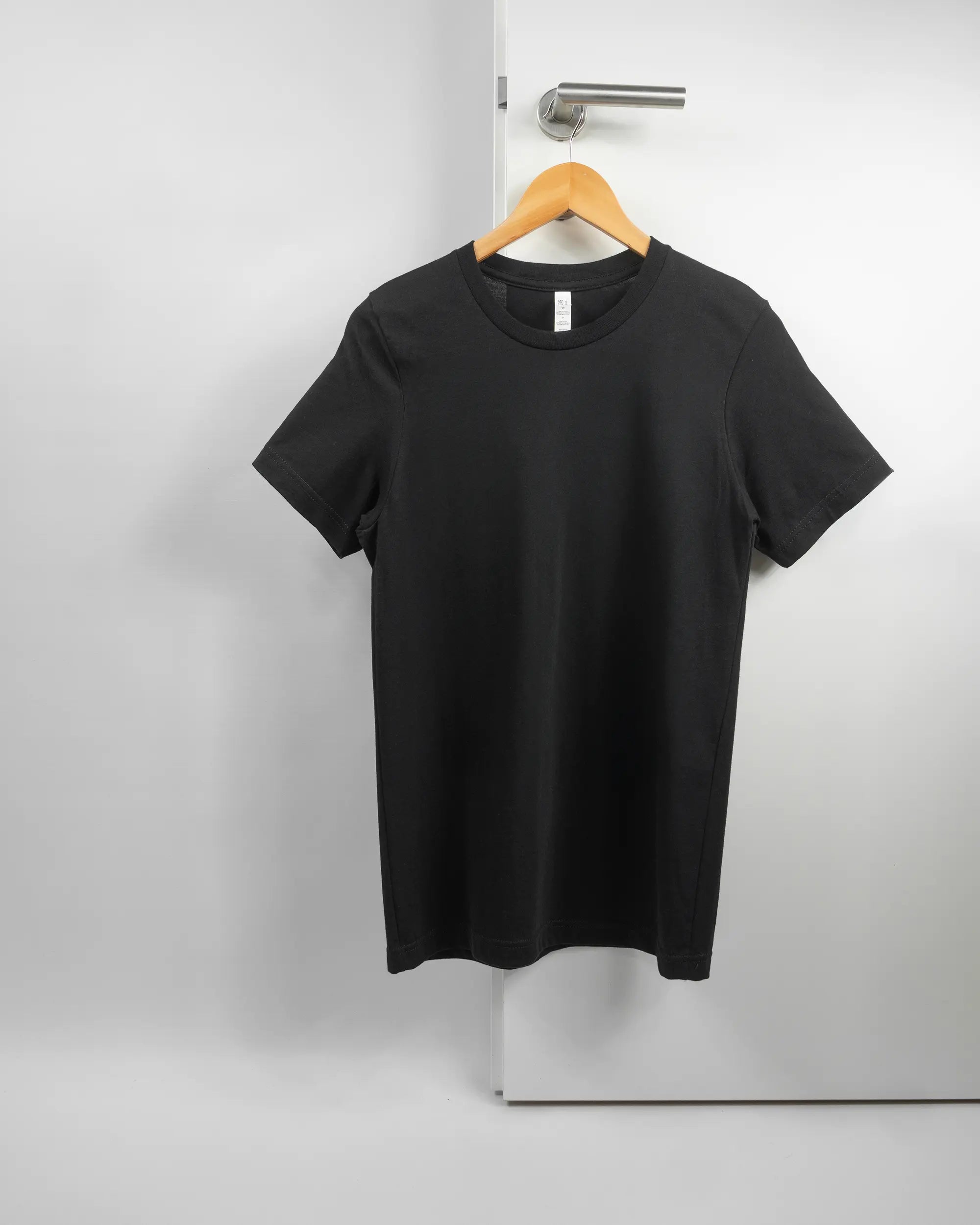 Vorderseite des Basic Unisex T-Shirt Light von Maondo ohne Motiv in der Farbe Black und in der Größe S auf einem Bügel an der Türklinke aufgehängt