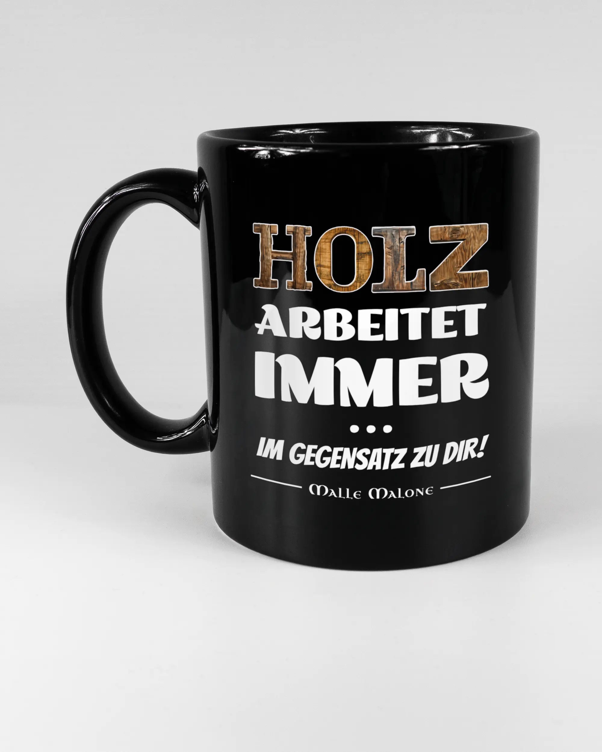 Titelbild, das die linke Seite der beidseitig bedruckten Keramiktasse von Maondo mit dem Design Holzarbeit in der Farbe Black auf einem Holztisch zeigt