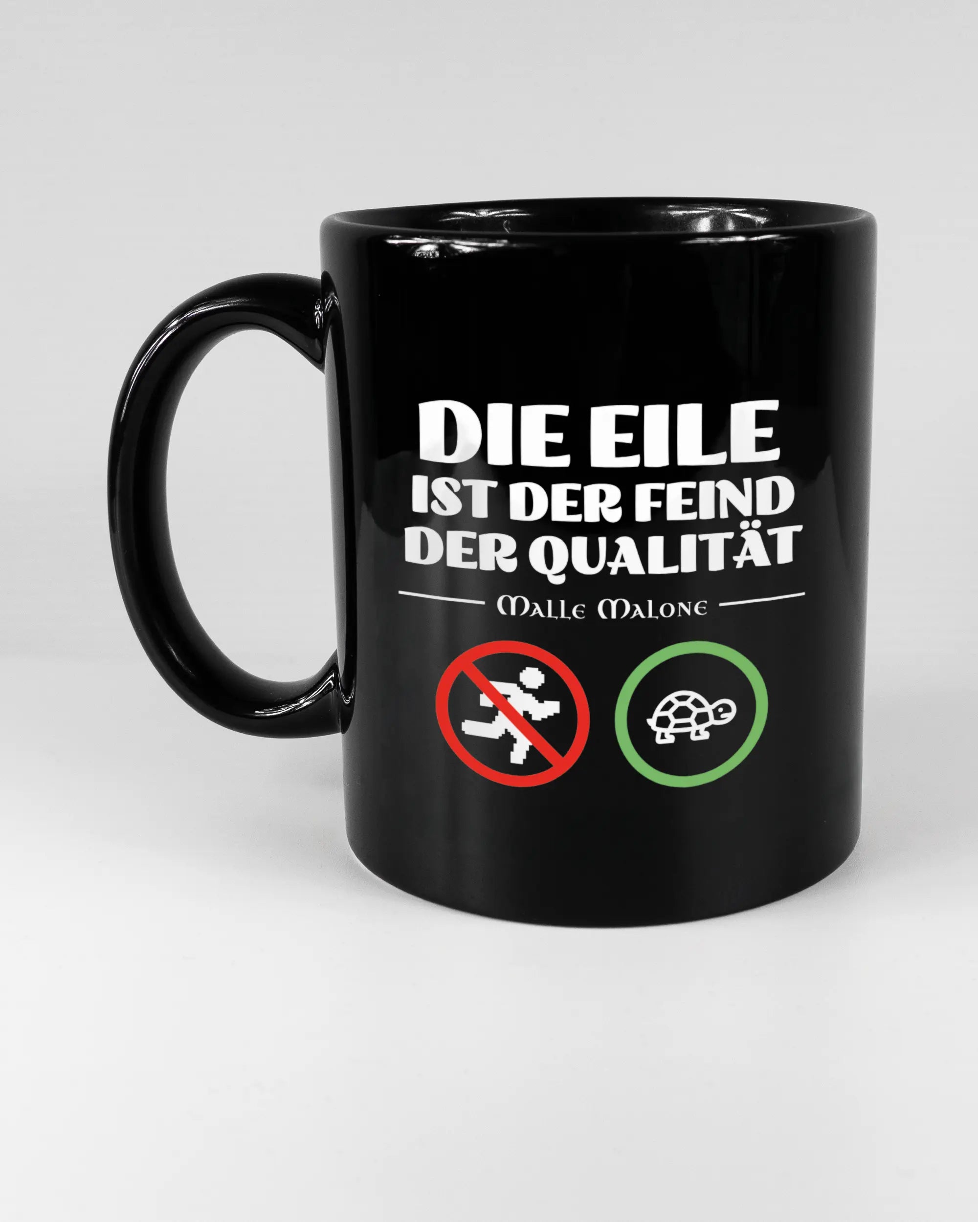 Titelbild, das die linke Seite der beidseitig bedruckten Keramiktasse von Maondo mit dem Design Keine Eile in der Farbe Black auf einem Holztisch zeigt