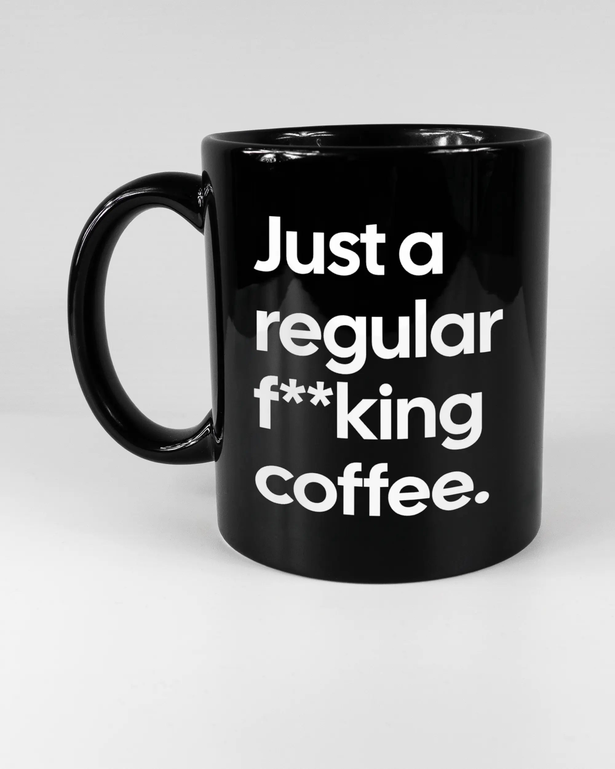 Titelbild, das die linke Seite der beidseitig bedruckten Keramiktasse von Maondo mit dem Design Regular Coffee in der Farbe Black auf einem Holztisch zeigt