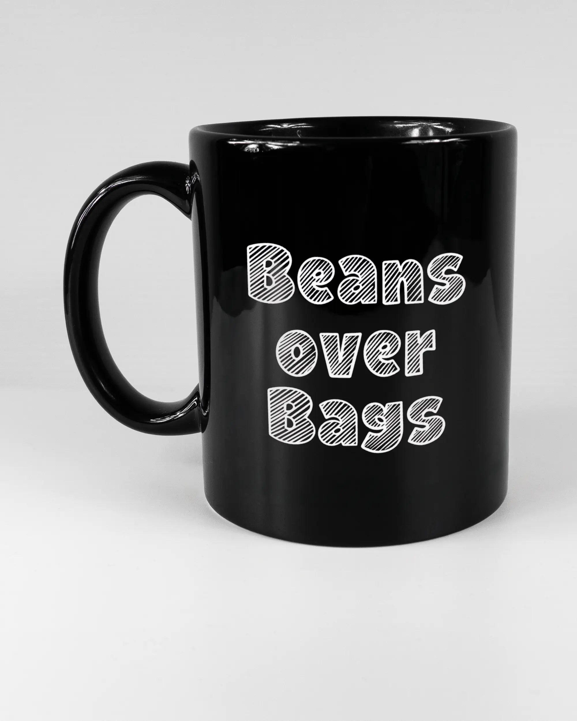 Titelbild, das die linke Seite der beidseitig bedruckten Keramiktasse von Maondo mit dem Design Beans over Bags in der Farbe Black auf einem Holztisch zeigt