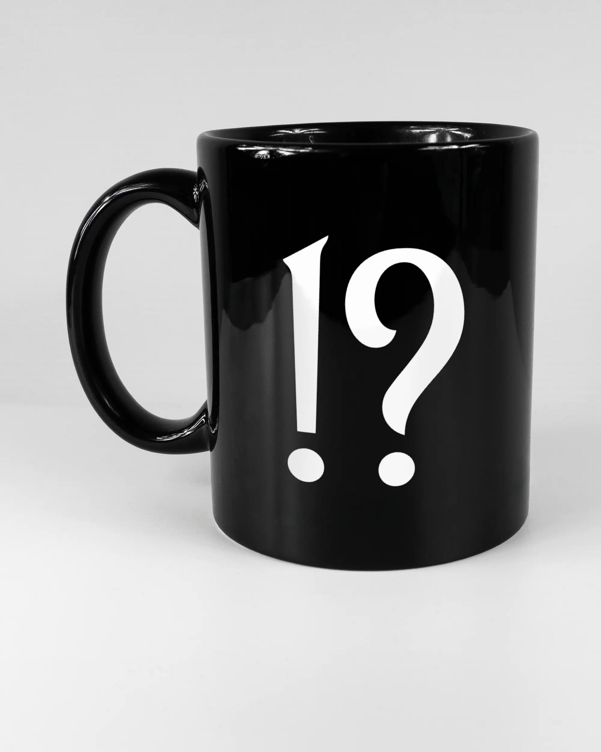 Titelbild, das die linke Seite der beidseitig bedruckten Keramiktasse von Maondo mit dem Design WHAT in der Farbe Black auf einem Holztisch zeigt