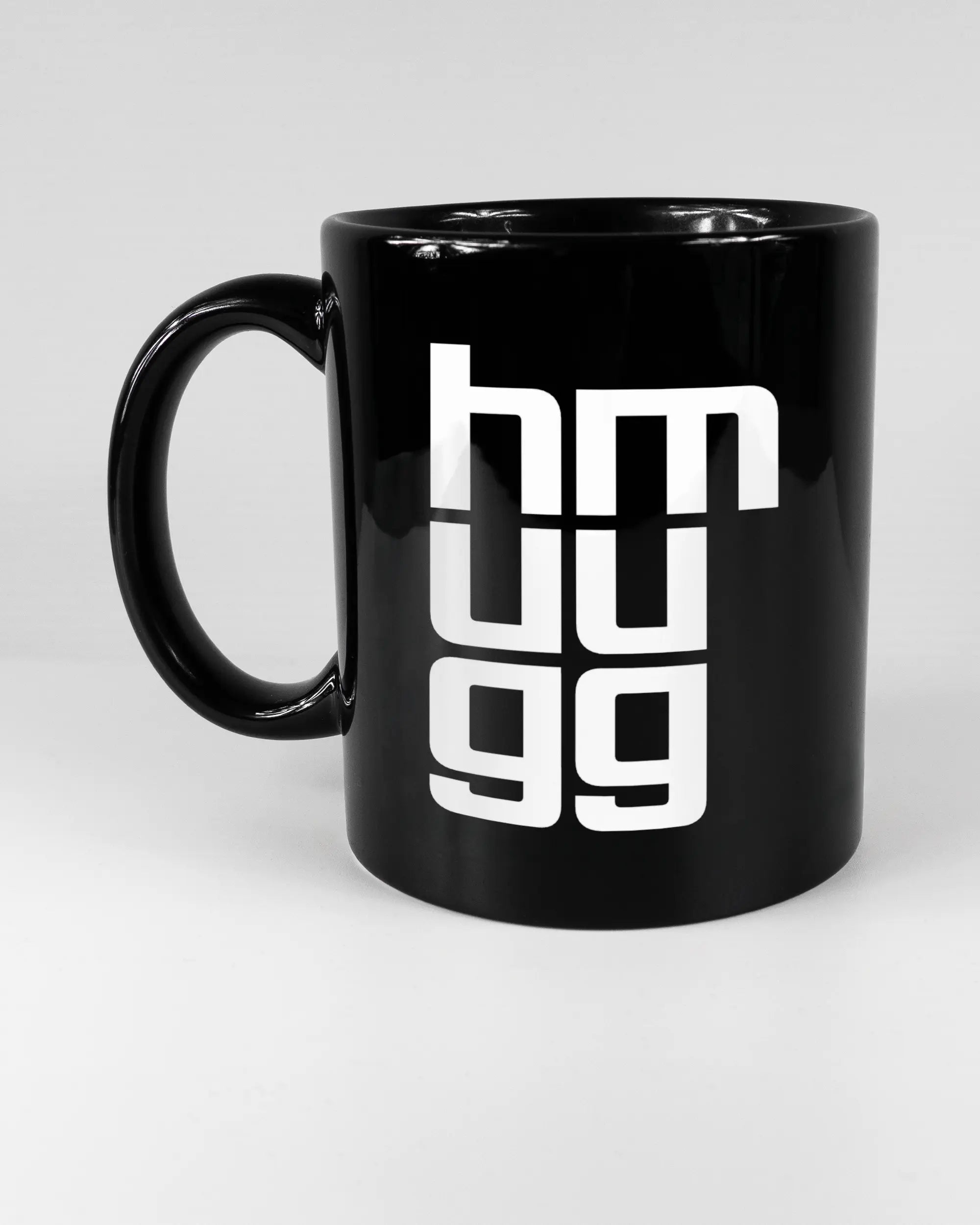 Titelbild, das die linke Seite der beidseitig bedruckten Keramiktasse von Maondo mit dem Design Hug Mug in der Farbe Black auf einem Holztisch zeigt
