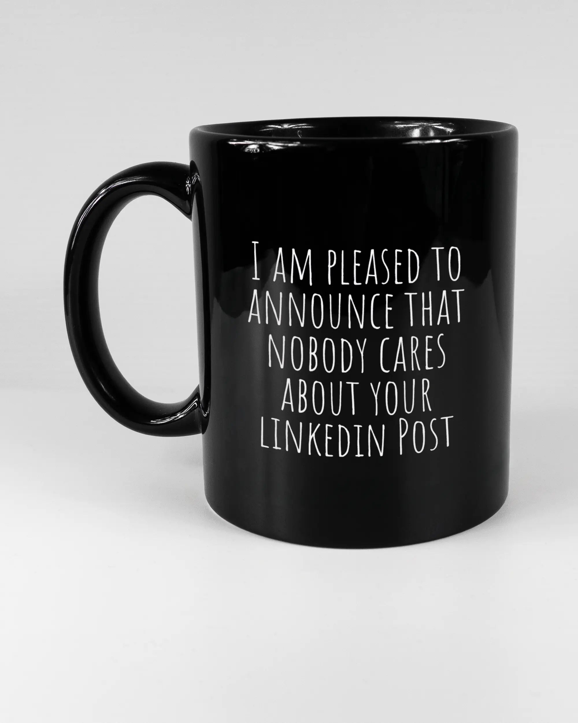 Titelbild, das die linke Seite der beidseitig bedruckten Keramiktasse von Maondo mit dem Design Please Unannounce in der Farbe Black auf einem Holztisch zeigt