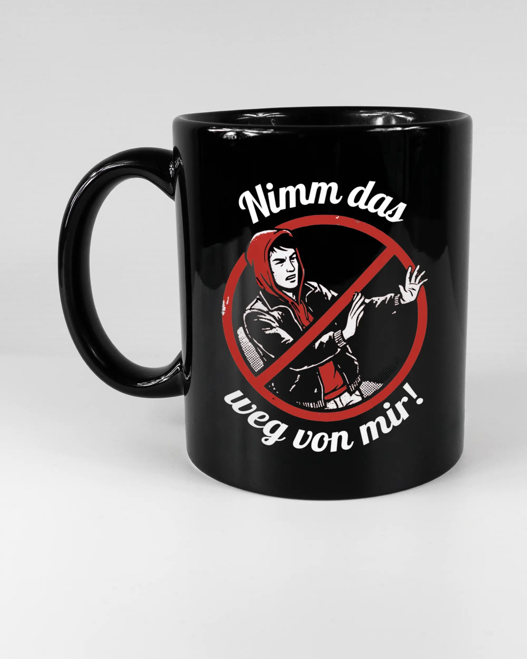 Titelbild, das die linke Seite der beidseitig bedruckten Keramiktasse von Maondo mit dem Design Nimm das weg in der Farbe Black auf einem Holztisch zeigt