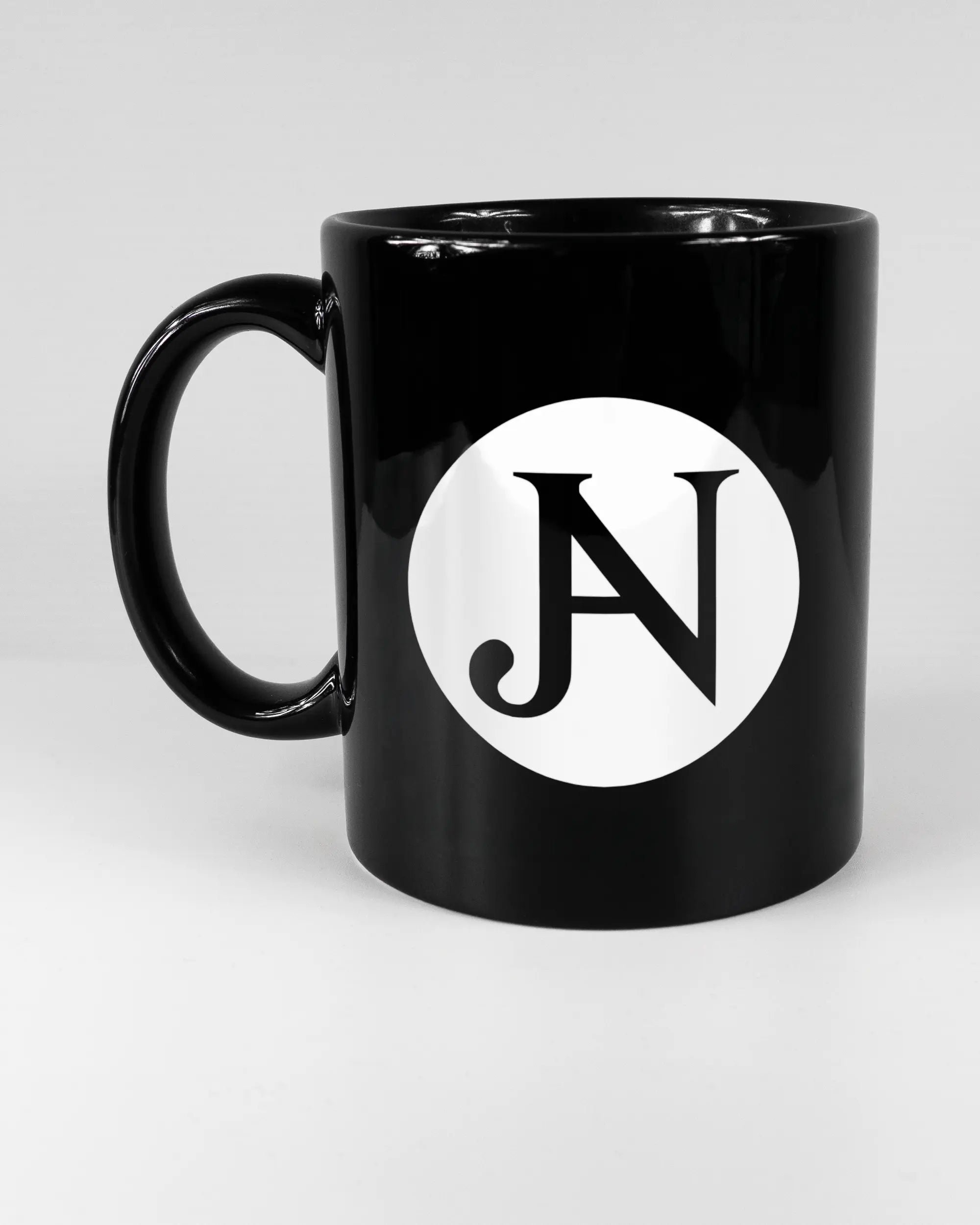 Titelbild, das die linke Seite der beidseitig bedruckten Keramiktasse von Maondo mit dem Design JB1 in der Farbe Black auf einem Holztisch zeigt