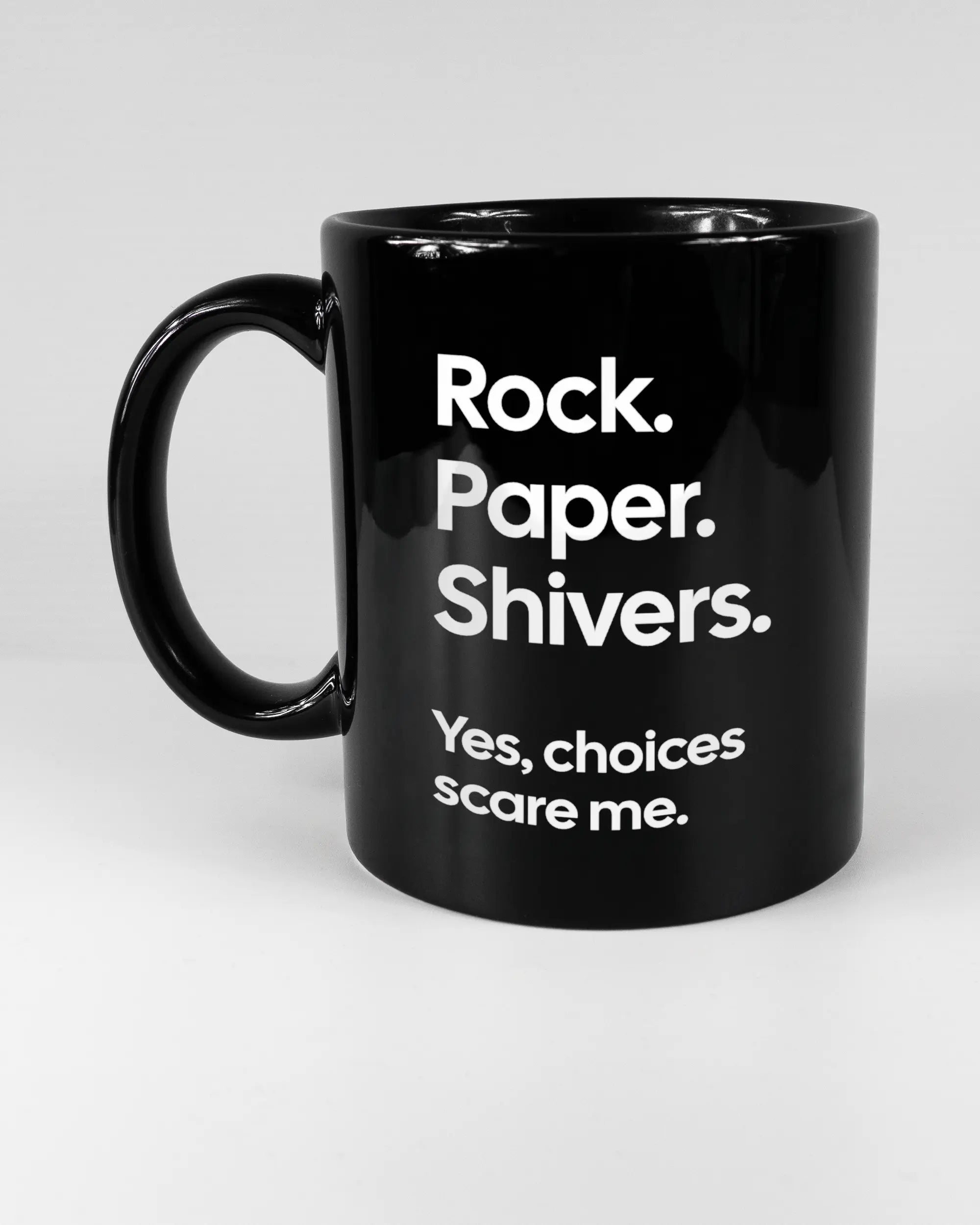 Titelbild, das die linke Seite der beidseitig bedruckten Keramiktasse von Maondo mit dem Design Rock Paper Shivers in der Farbe Black auf einem Holztisch zeigt