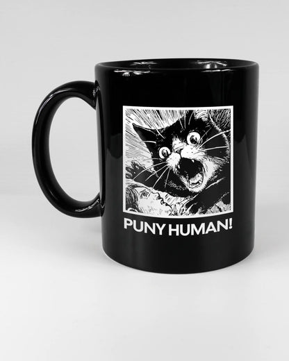 Titelbild, das die linke Seite der beidseitig bedruckten Keramiktasse von Maondo mit dem Design Puny Human in der Farbe Black auf einem Holztisch zeigt