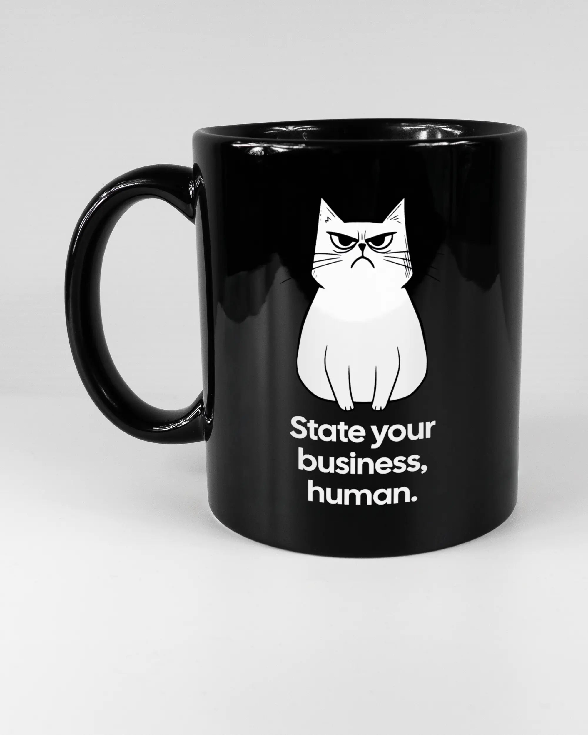 Titelbild, das die linke Seite der beidseitig bedruckten Keramiktasse von Maondo mit dem Design Grumpy Purr in der Farbe Black auf einem Holztisch zeigt