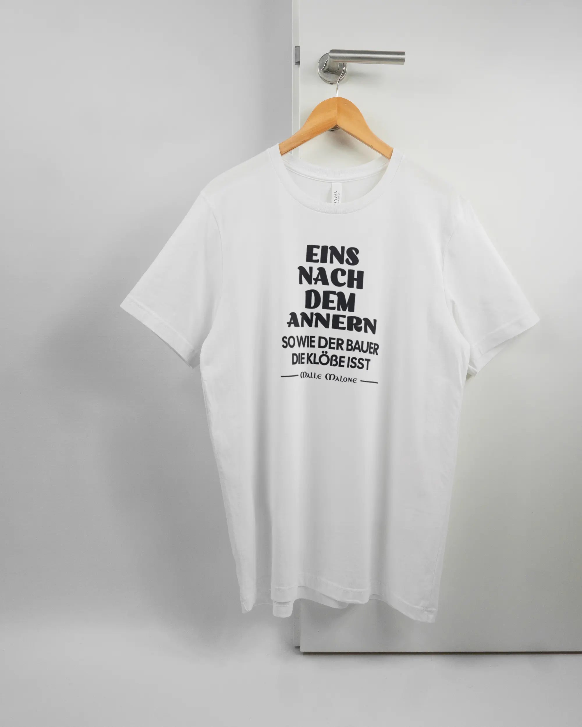 Vorderseite des Basic Unisex T-Shirt Light von Maondo mit dem Design Eins nach dem Annern in der Farbe White und in der Größe L auf einem Bügel an der Türklinke aufgehängt