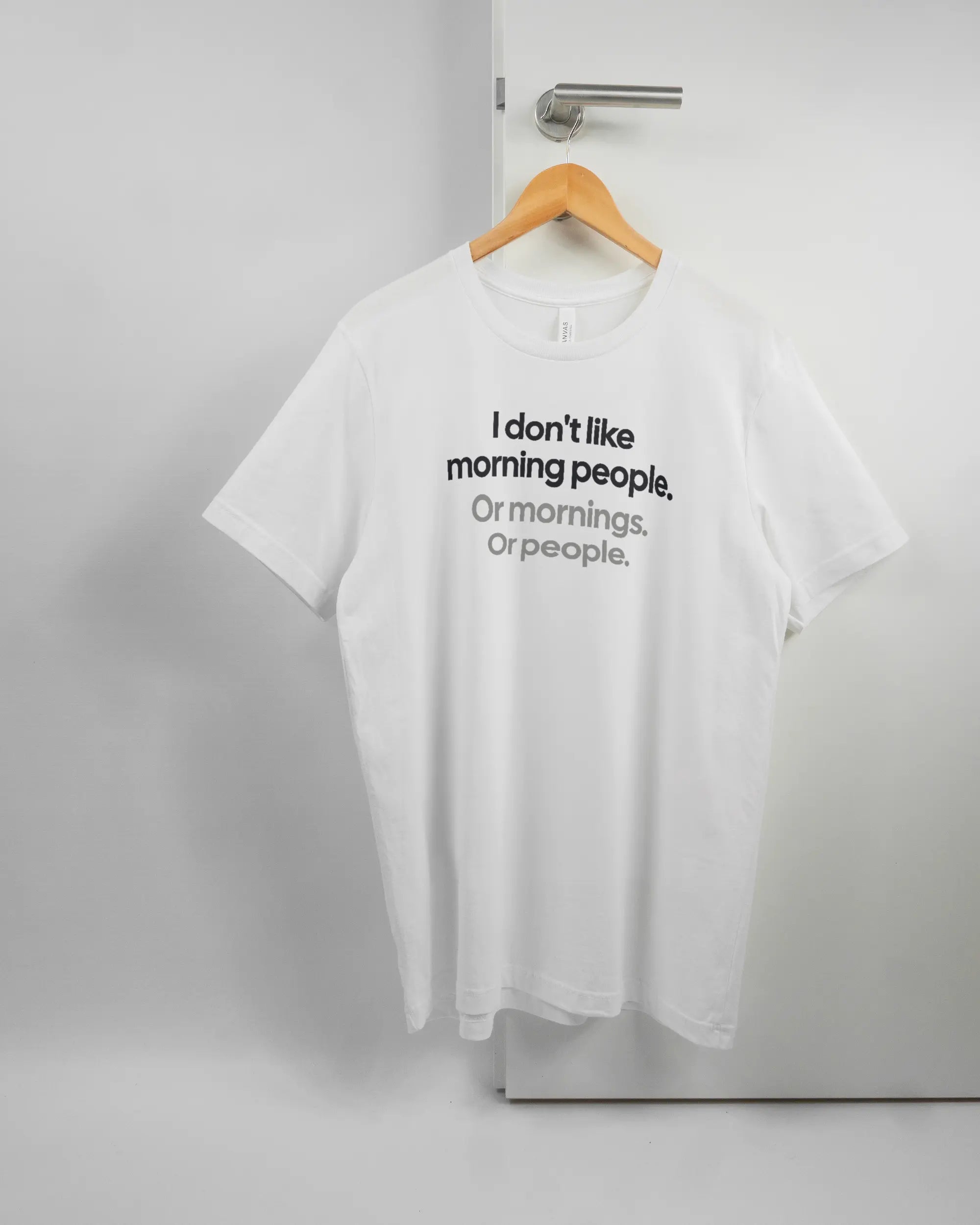 Vorderseite des Basic Unisex T-Shirt Light von Maondo mit dem Design Morning Person in der Farbe White und in der Größe L auf einem Bügel an der Türklinke aufgehängt