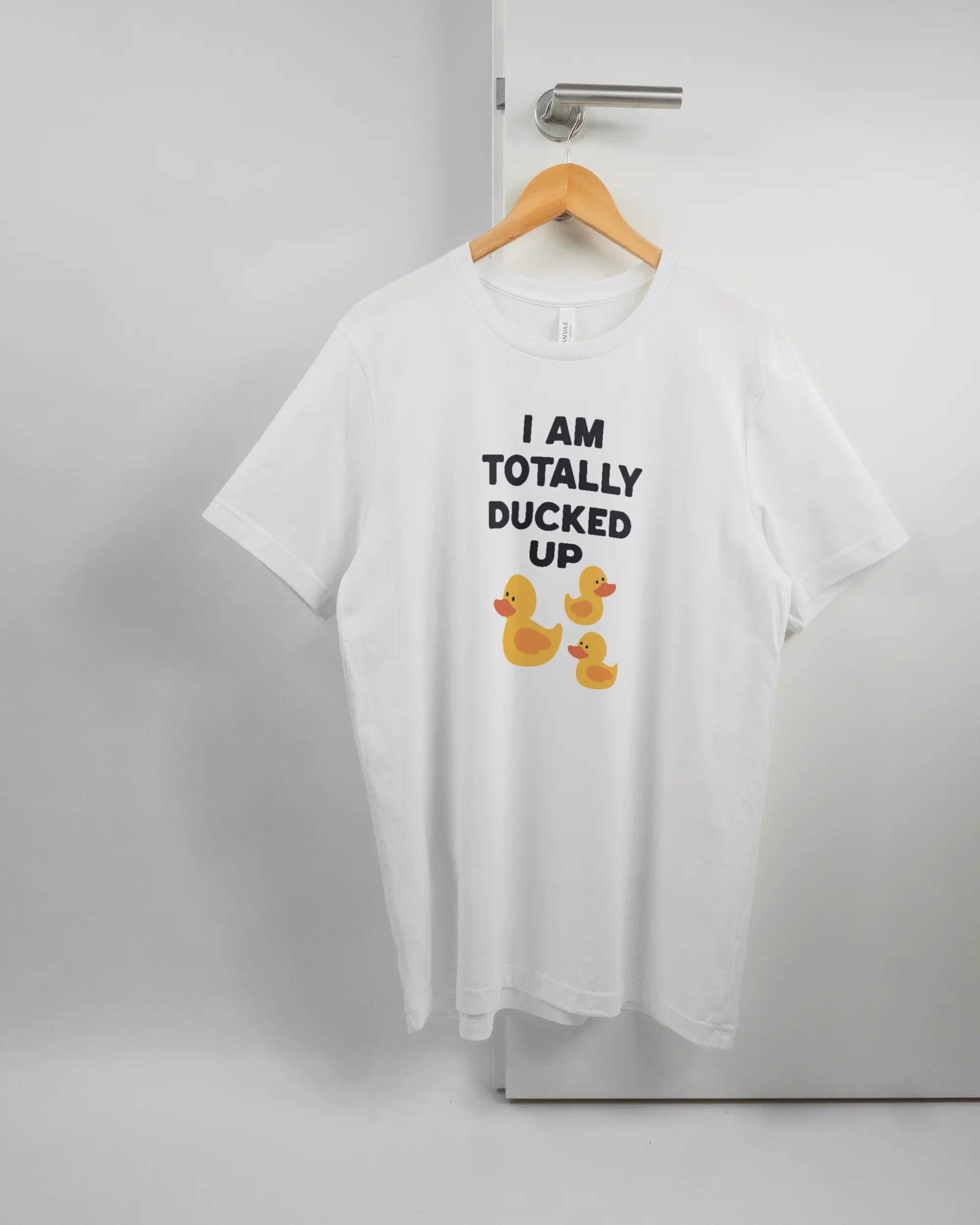 Vorderseite des Basic Unisex T-Shirt Light von Maondo mit dem Design Ducked Up in der Farbe White und in der Größe L auf einem Bügel an der Türklinke aufgehängt