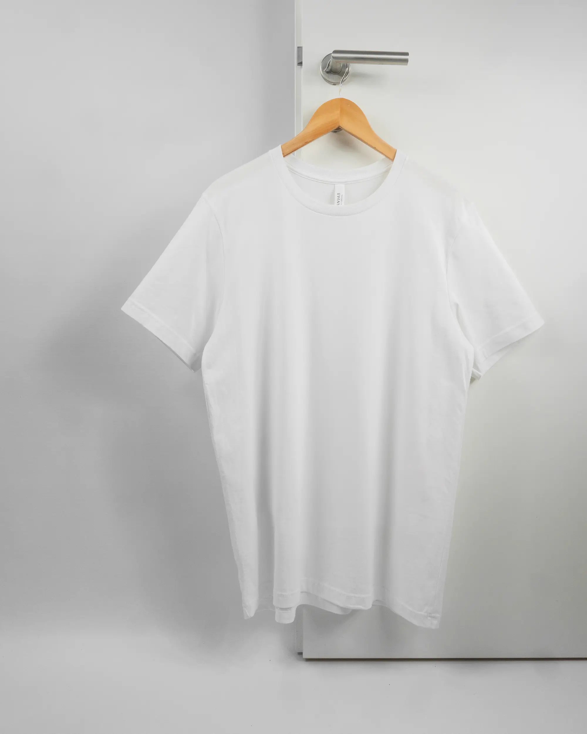Vorderseite des Basic Unisex T-Shirt Light von Maondo ohne Motiv in der Farbe White und in der Größe L auf einem Bügel an der Türklinke aufgehängt
