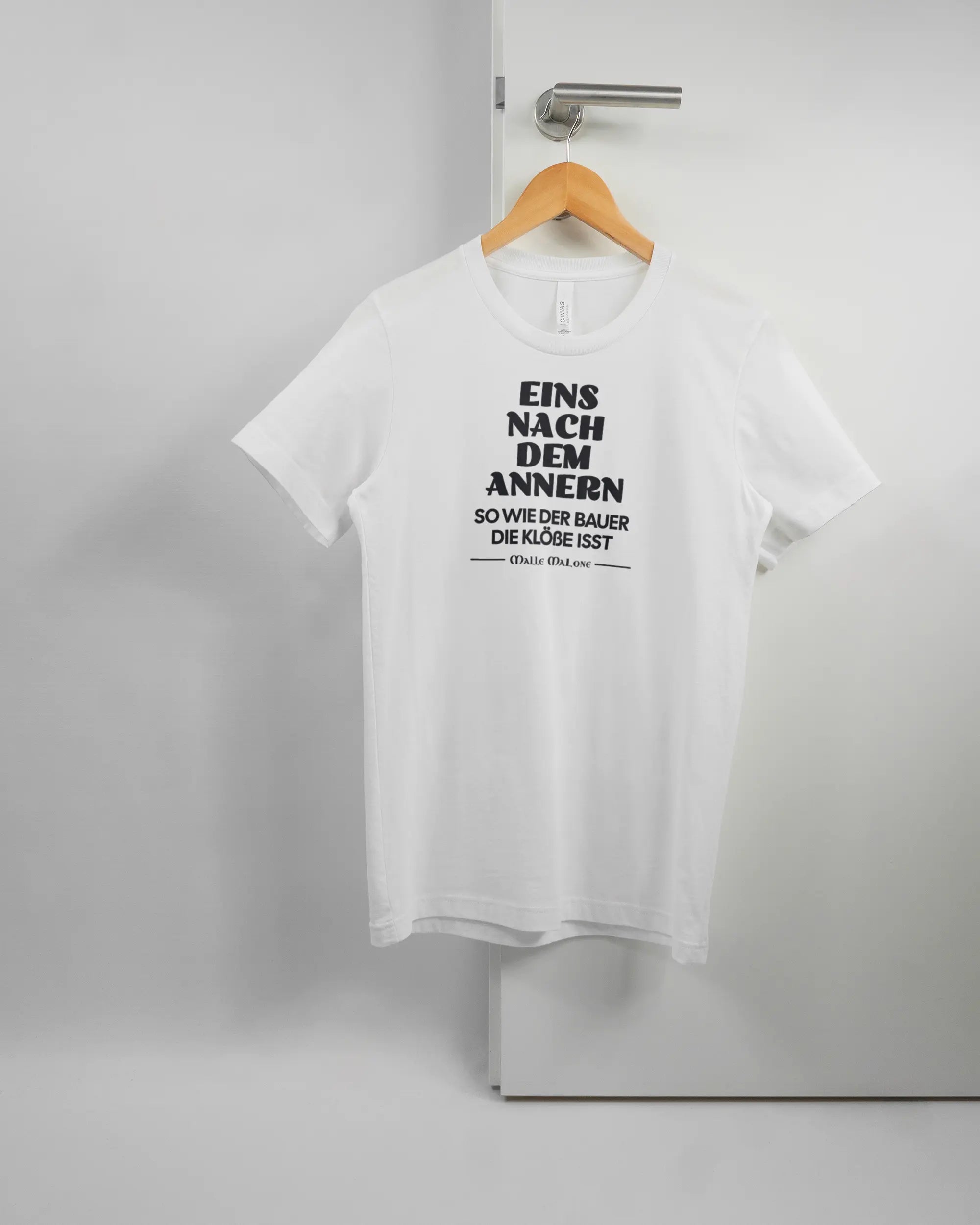 Vorderseite des Basic Unisex T-Shirt Light von Maondo mit dem Design Eins nach dem Annern in der Farbe White und in der Größe S auf einem Bügel an der Türklinke aufgehängt