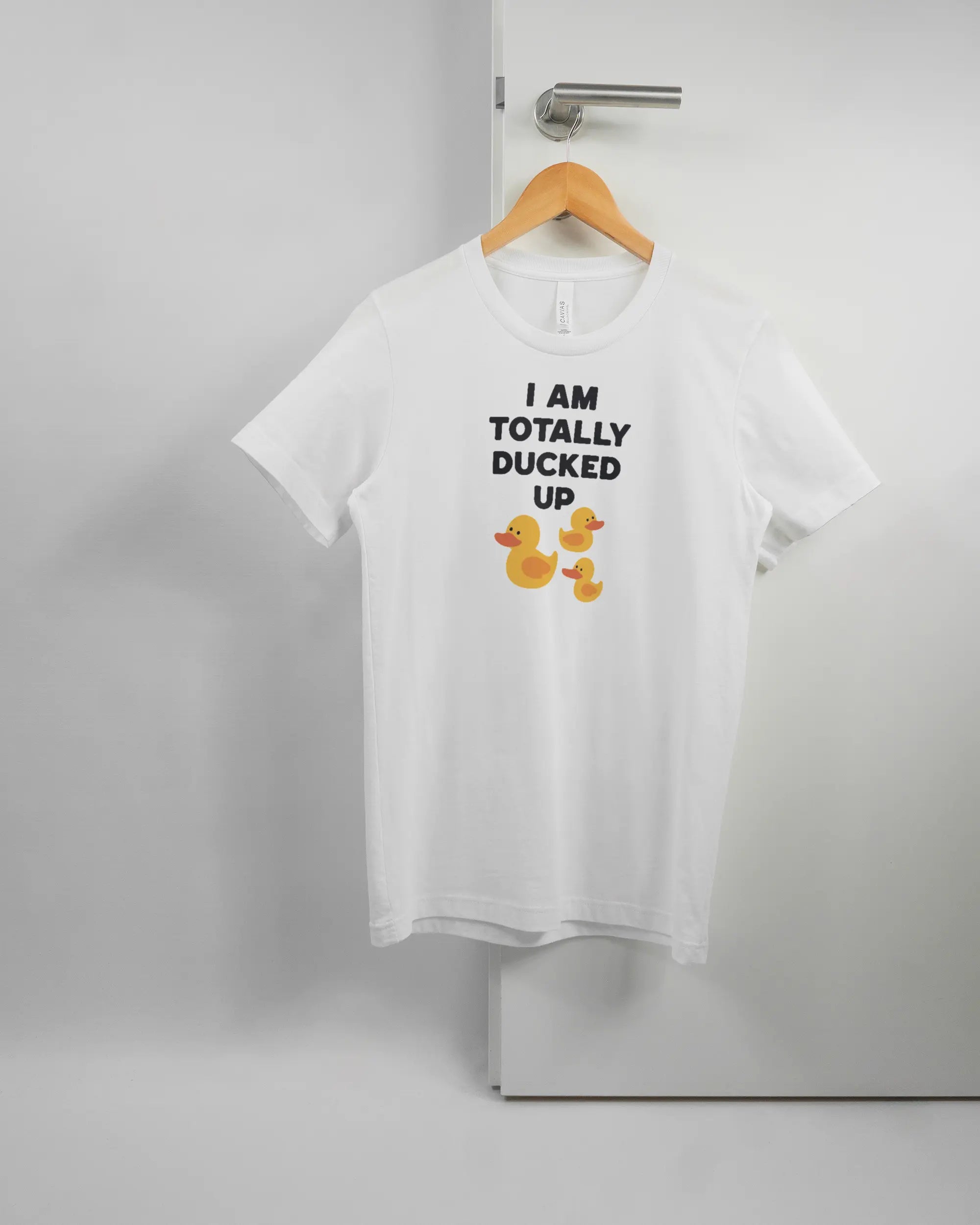 Vorderseite des Basic Unisex T-Shirt Light von Maondo mit dem Design Ducked Up in der Farbe White und in der Größe S auf einem Bügel an der Türklinke aufgehängt