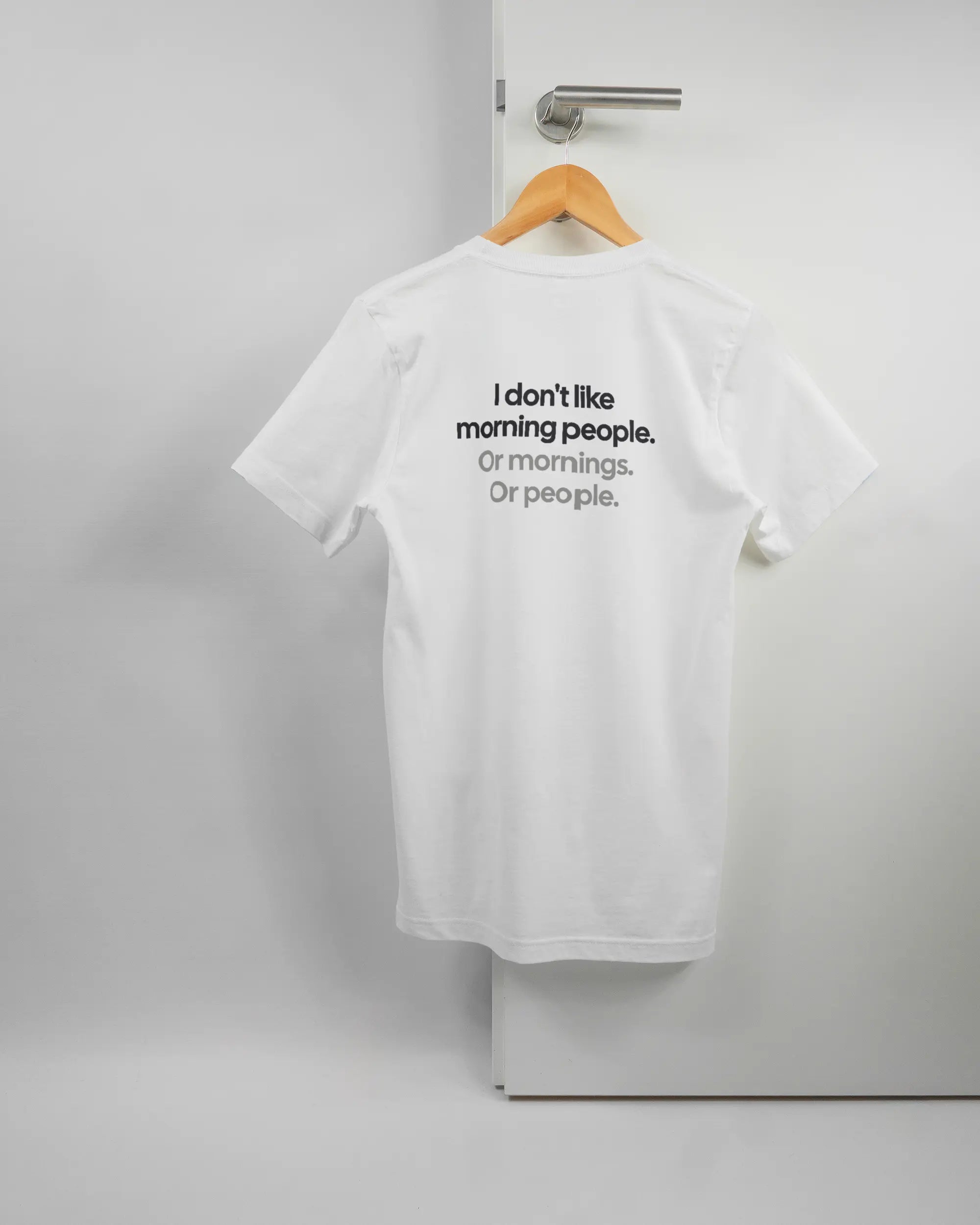 Rückseite des Basic Unisex T-Shirt Light von Maondo mit dem Design Morning Person in der Farbe White und in der Größe S auf einem Bügel an der Türklinke aufgehängt