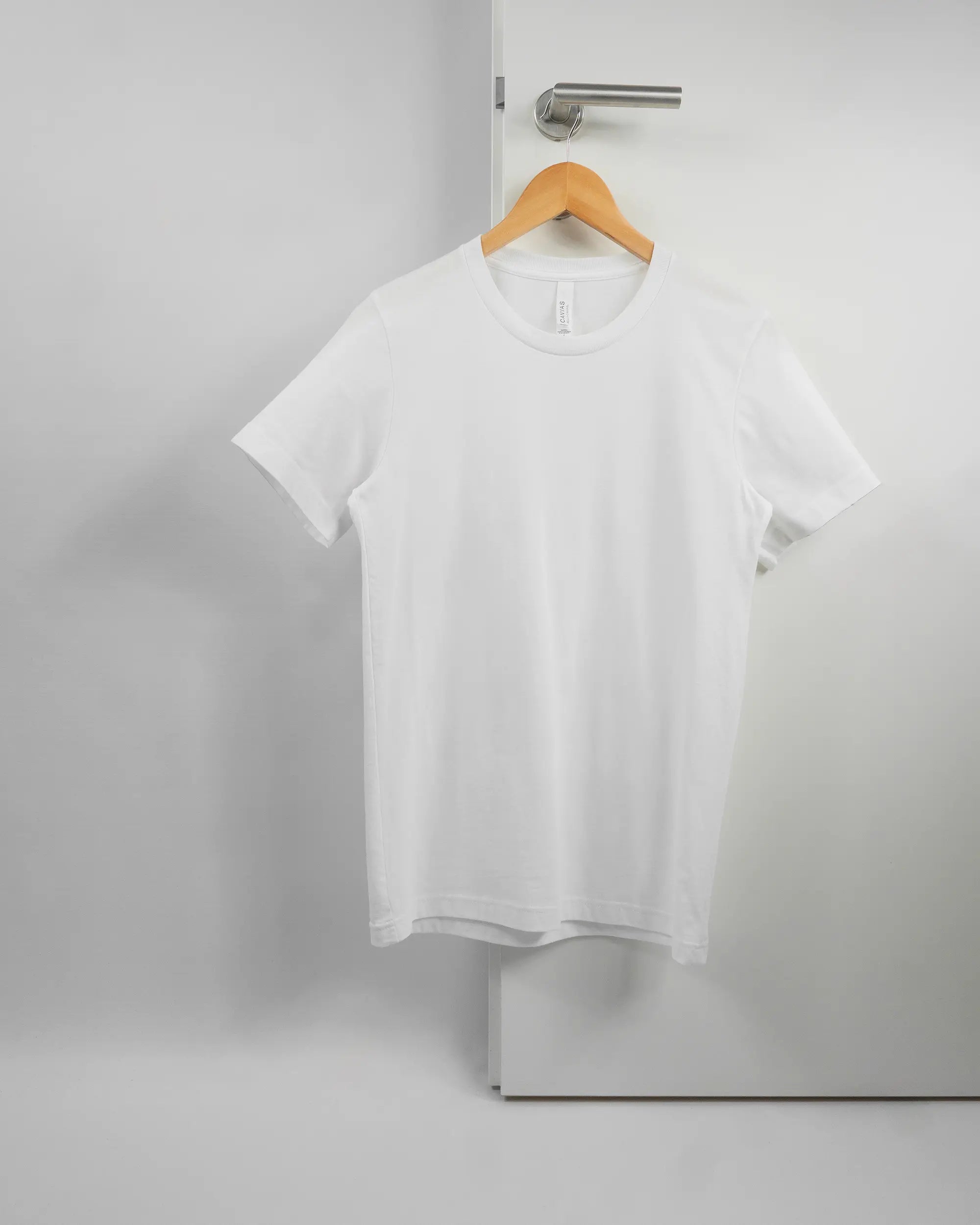 Vorderseite des Basic Unisex T-Shirt Light von Maondo ohne Motiv in der Farbe White und in der Größe S auf einem Bügel an der Türklinke aufgehängt
