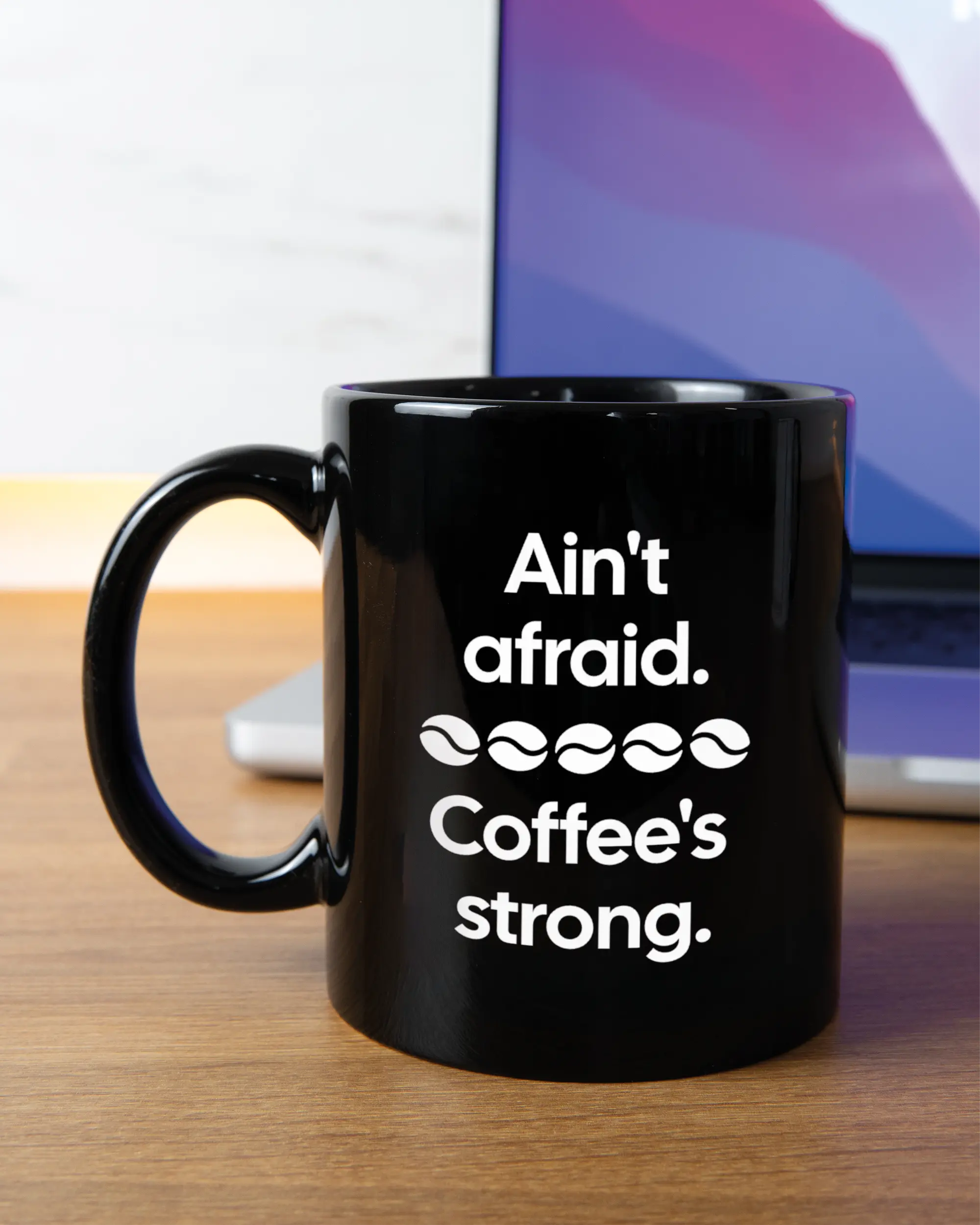 Homeoffice Aufnahme der linken Seite der beidseitig bedruckten Keramiktasse von Maondo mit dem Design Coffee is strong in der Farbe Black