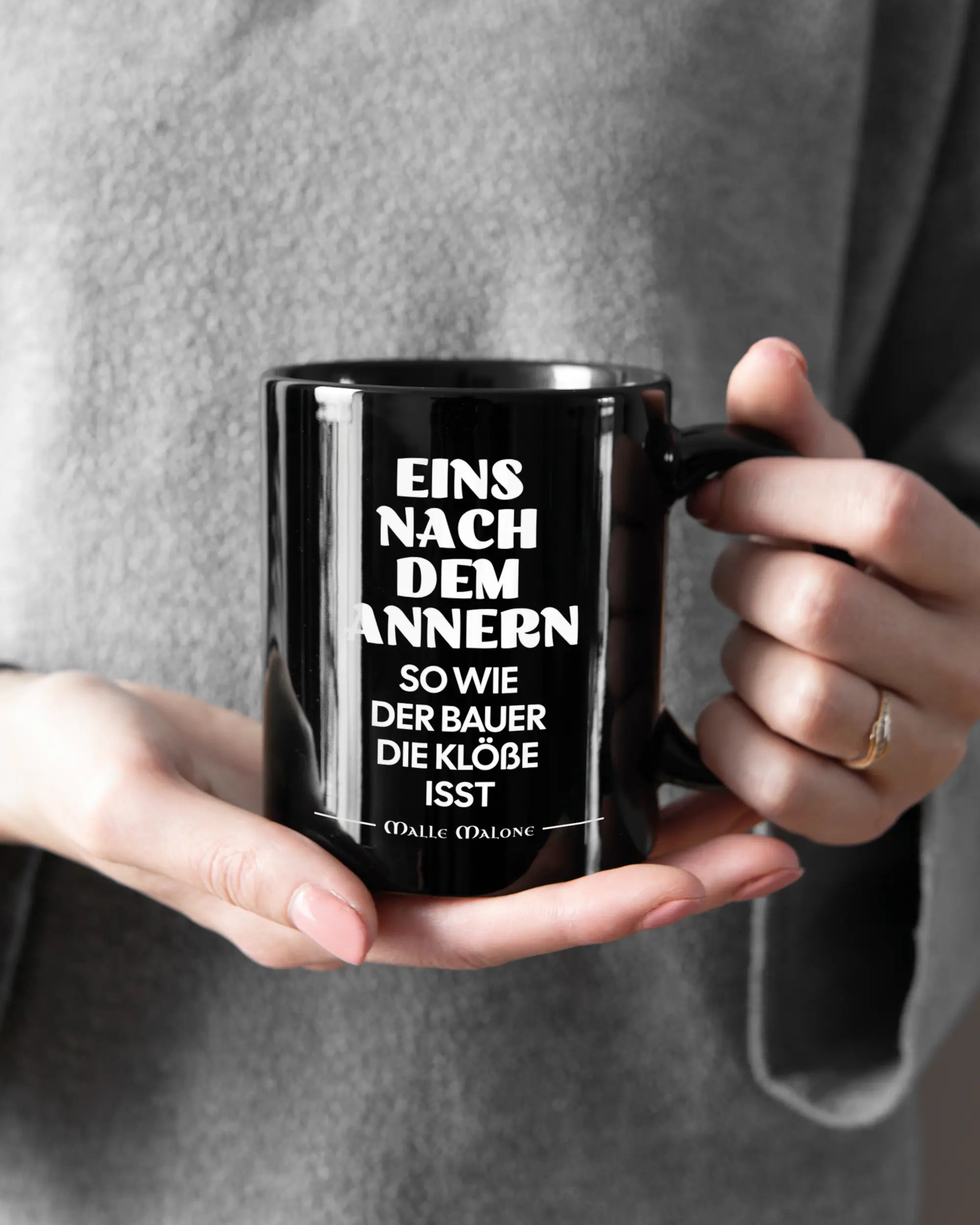 Rechte Seite der beidseitig bedruckten Keramiktasse von Maondo mit dem Design Eins nach dem Annern in der Farbe Black gehalten von Frauenhänden