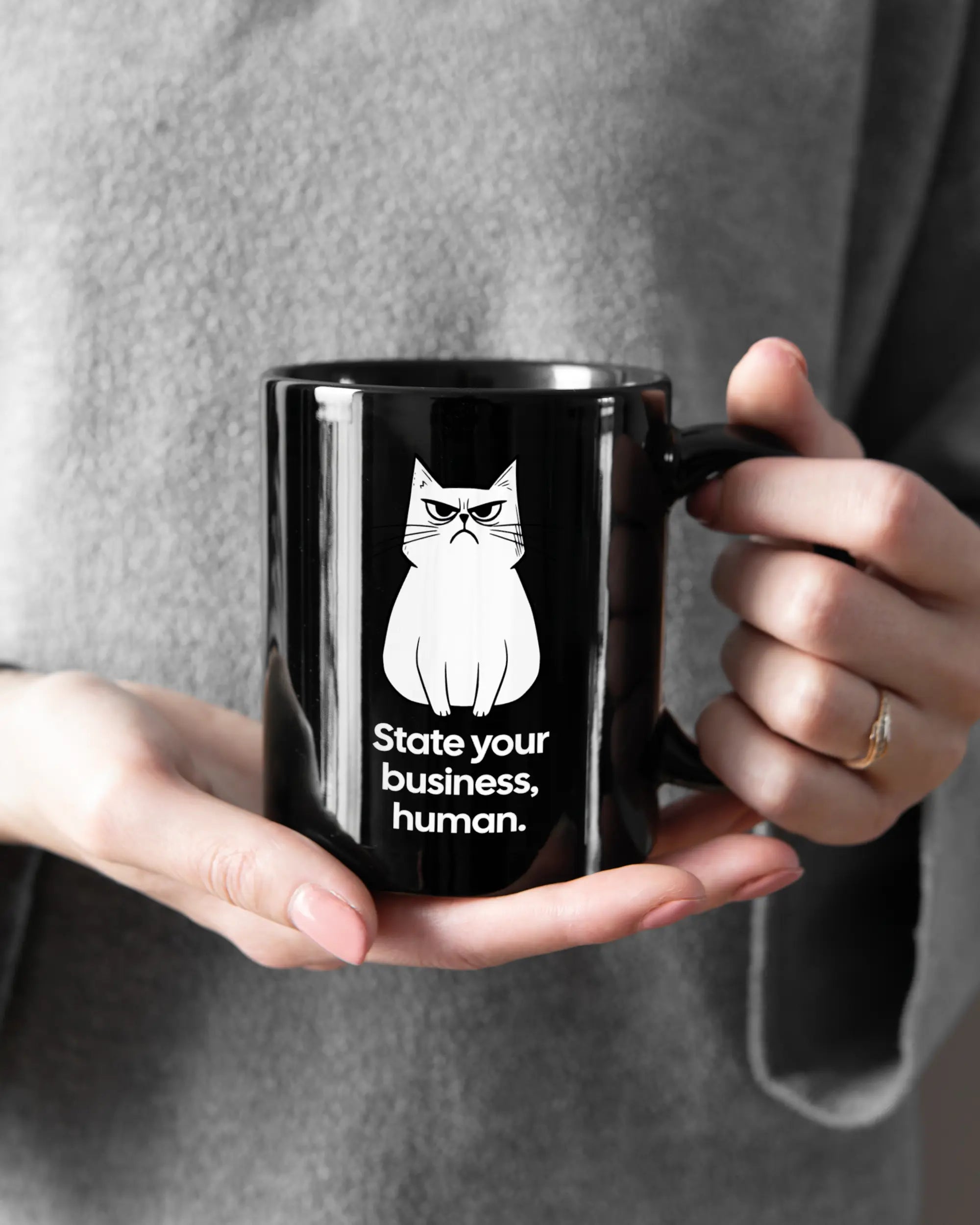 Rechte Seite der beidseitig bedruckten Keramiktasse von Maondo mit dem Design Grumpy Purr in der Farbe Black gehalten von Frauenhänden