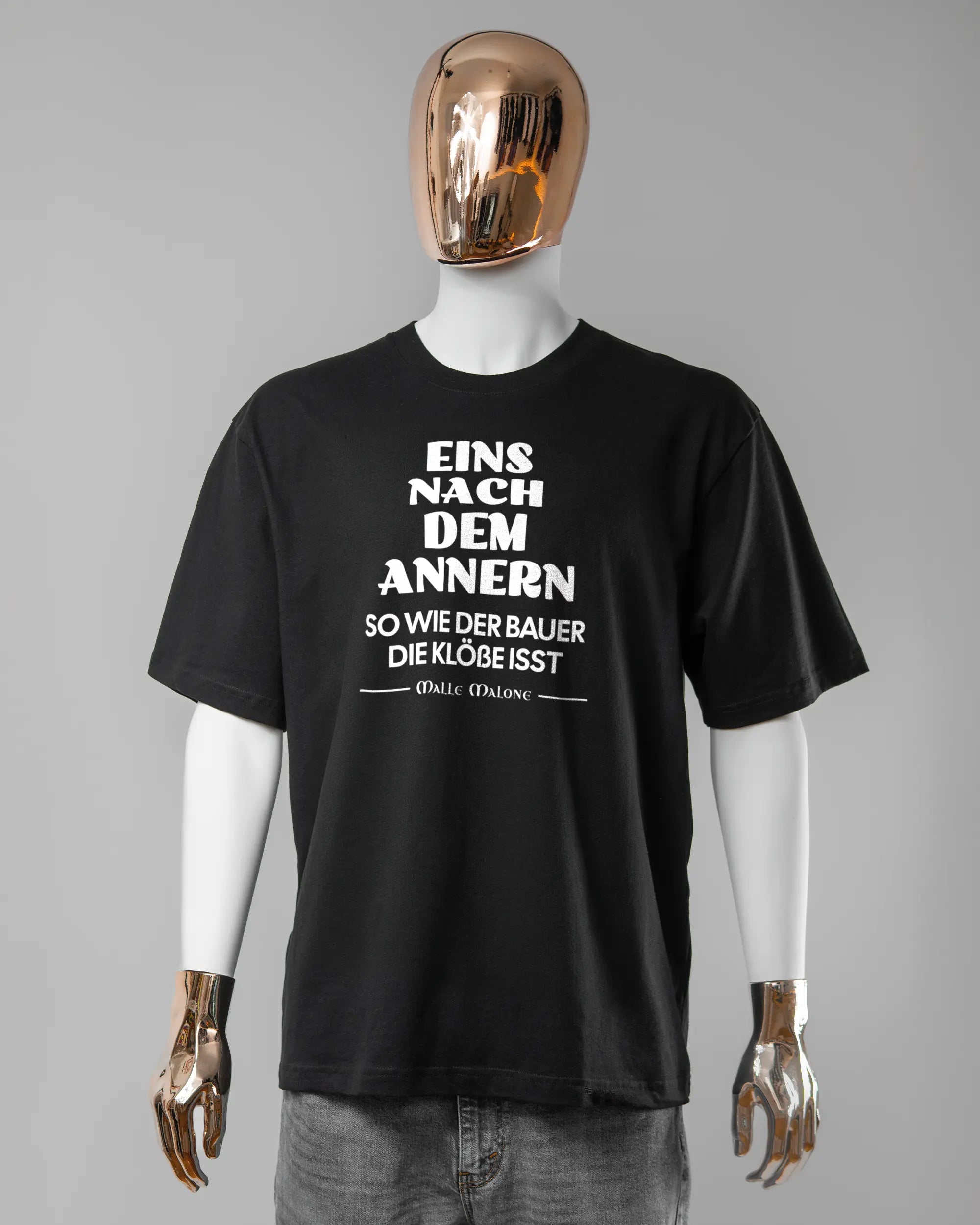 Vorderseite des Basic Unisex T-Shirt Oversized von Maondo mit dem Design Eins nach dem Annern in der Farbe Black und in der Größe L getragen von einer maskulinen Puppe