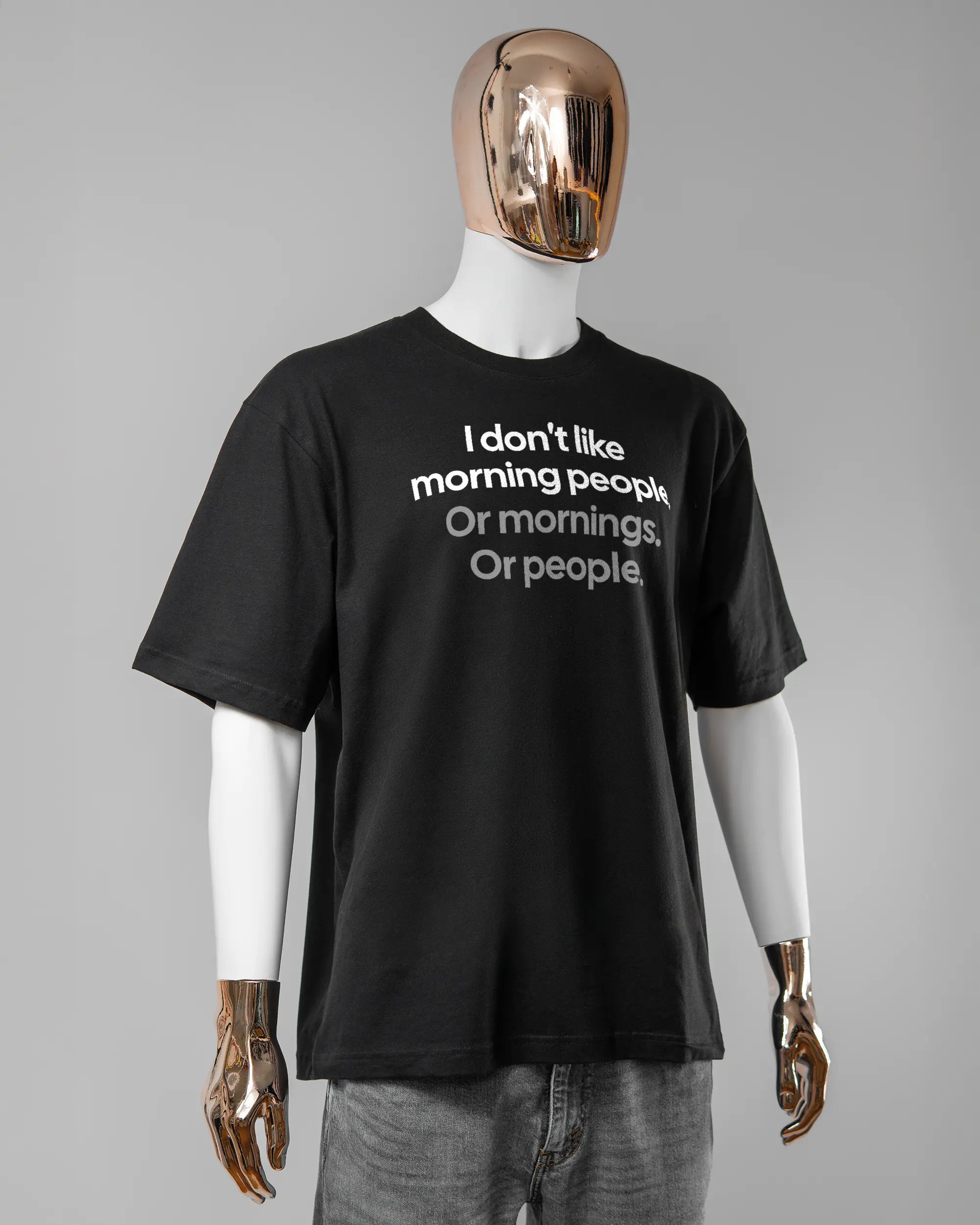 Vorderseite des Basic Unisex T-Shirt Oversized von Maondo mit dem Design Morning Person in der Farbe Black und in der Größe L getragen von einer maskulinen Puppe