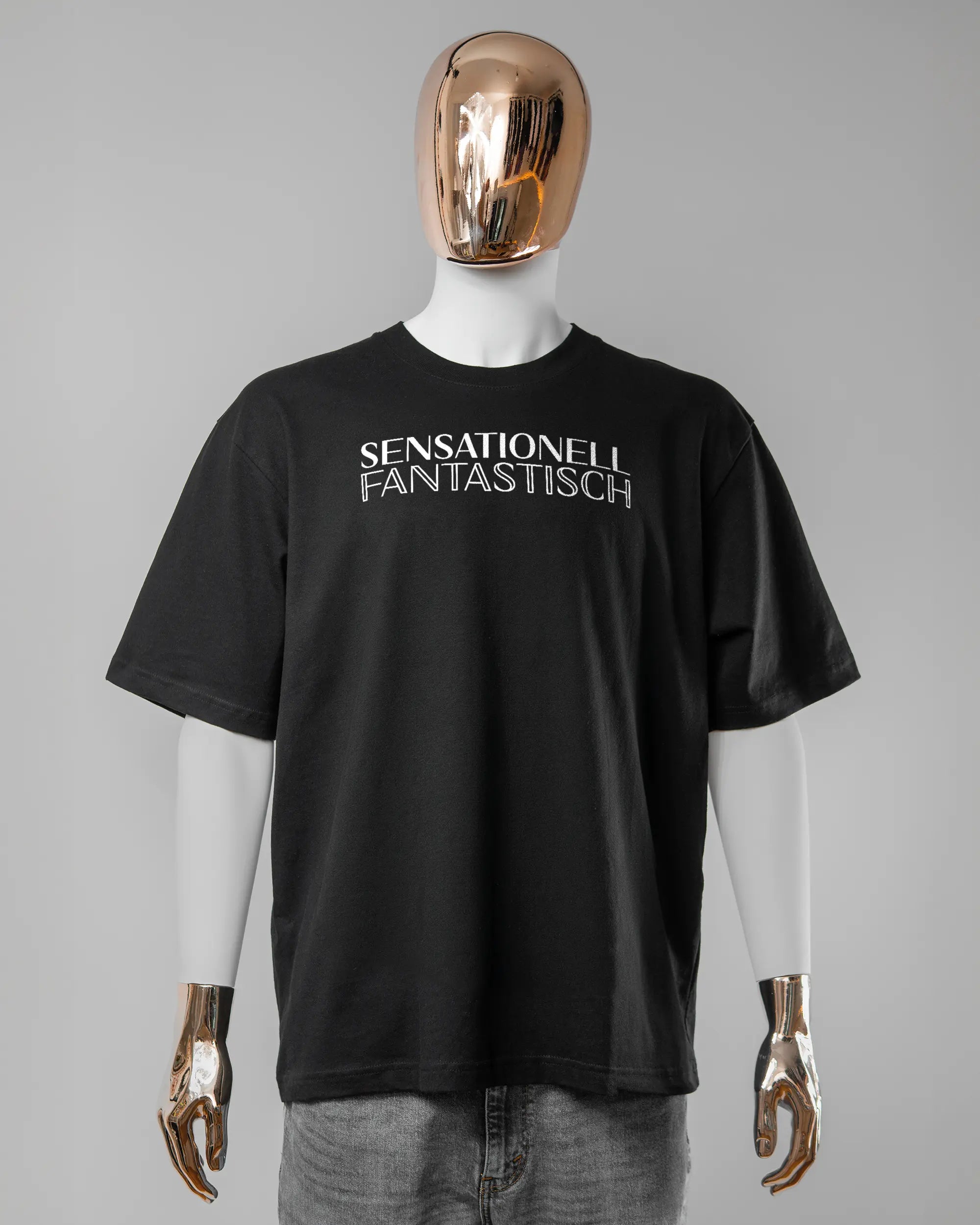 Vorderseite des Basic Unisex T-Shirt Oversized von Maondo mit dem Design Sensationell in der Farbe Black und in der Größe L getragen von einer maskulinen Puppe