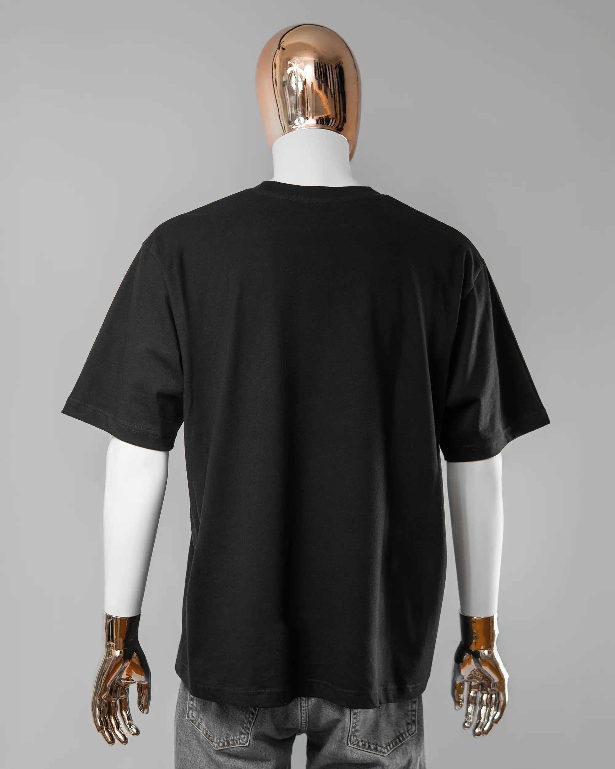 Rückseite des Basic Unisex T-Shirt Oversized von Maondo ohne Motiv in der Farbe Black und in der Größe L getragen von einer maskulinen Puppe