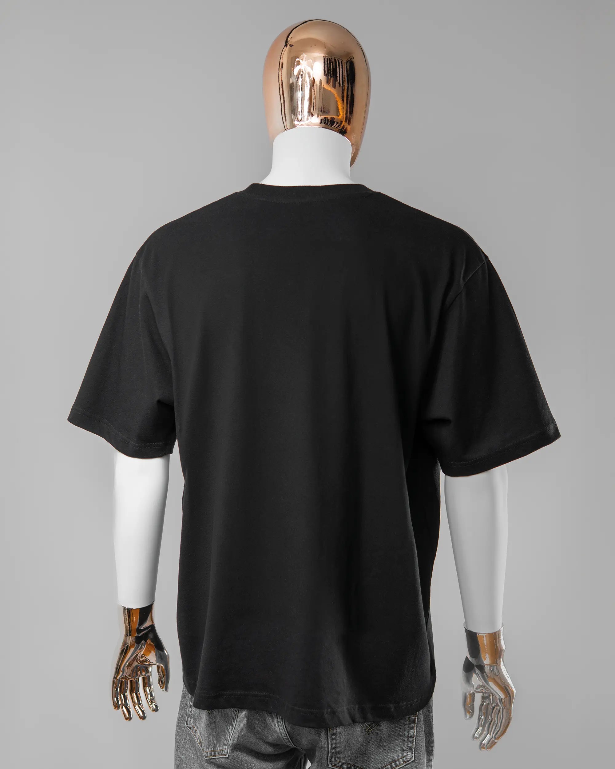 Rückseite des Basic Unisex T-Shirt Oversized von Maondo ohne Motiv in der Farbe Black und in der Größe L getragen von einer maskulinen Puppe