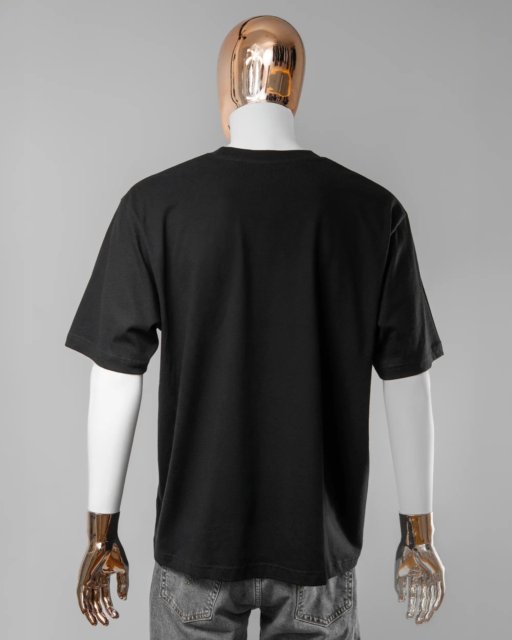 Rückseite des Basic Unisex T-Shirt Oversized von Maondo ohne Motiv in der Farbe Black und in der Größe L getragen von einer maskulinen Puppe