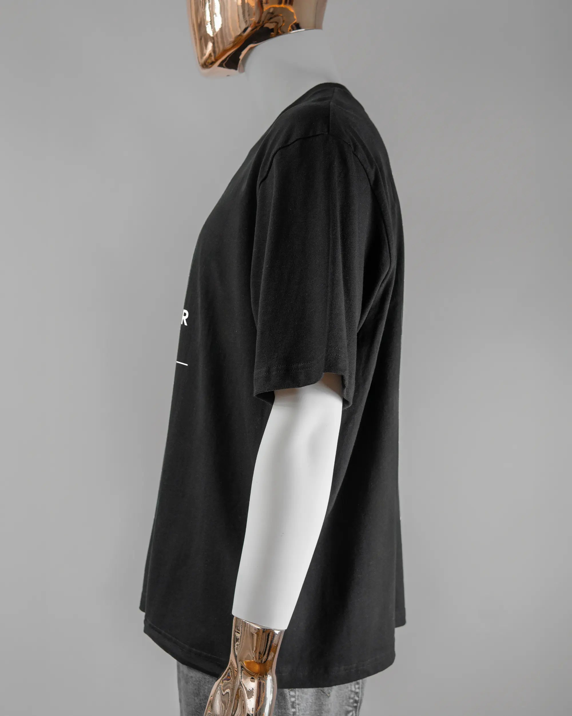 Seitenansicht des Basic Unisex T-Shirt Oversized von Maondo mit dem Design Eins nach dem Annern vorne in der Farbe Black und in der Größe L getragen von einer maskulinen Puppe