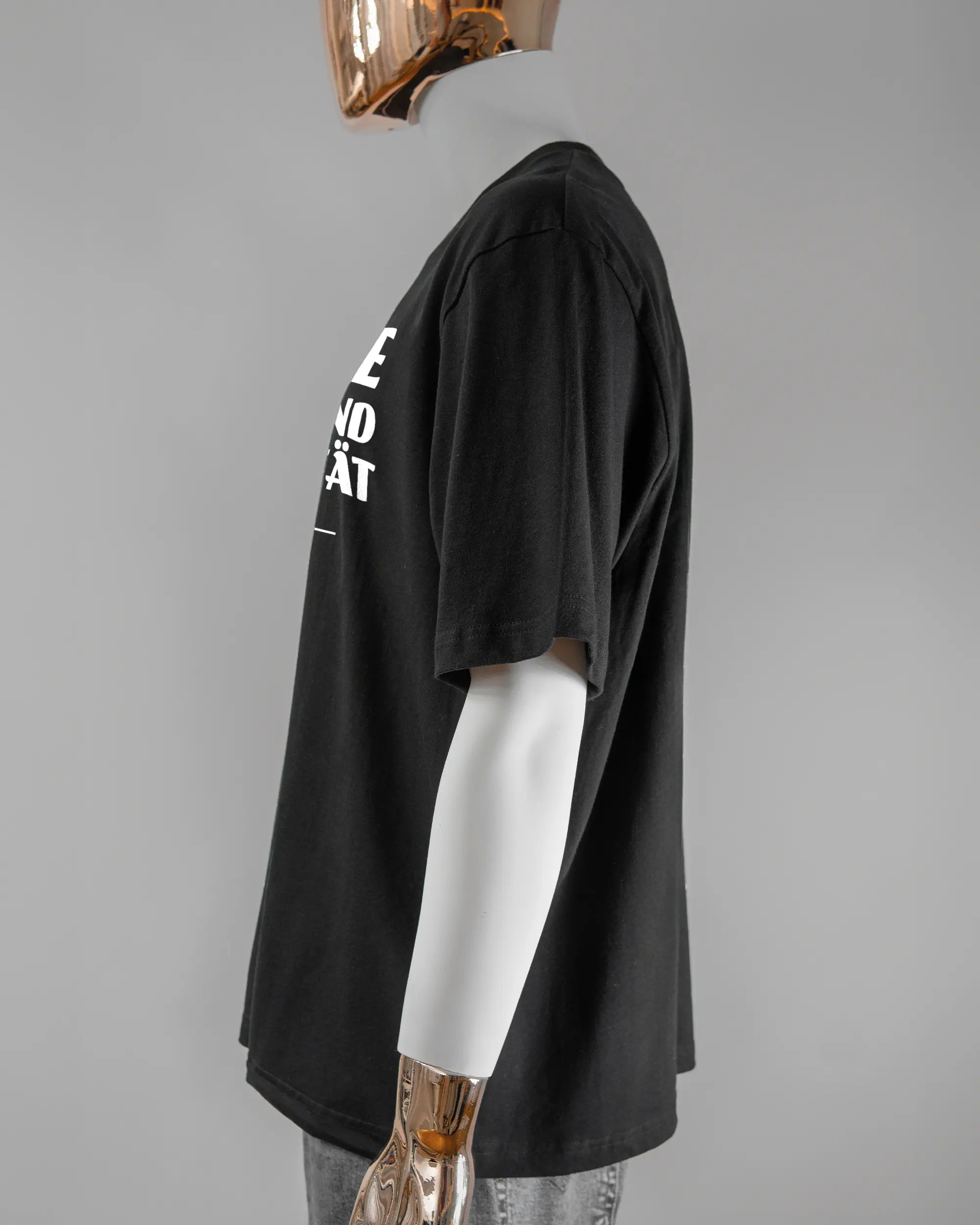 Seitenansicht des Basic Unisex T-Shirt Oversized von Maondo mit dem Design Keine Eile vorne in der Farbe Black und in der Größe L getragen von einer maskulinen Puppe