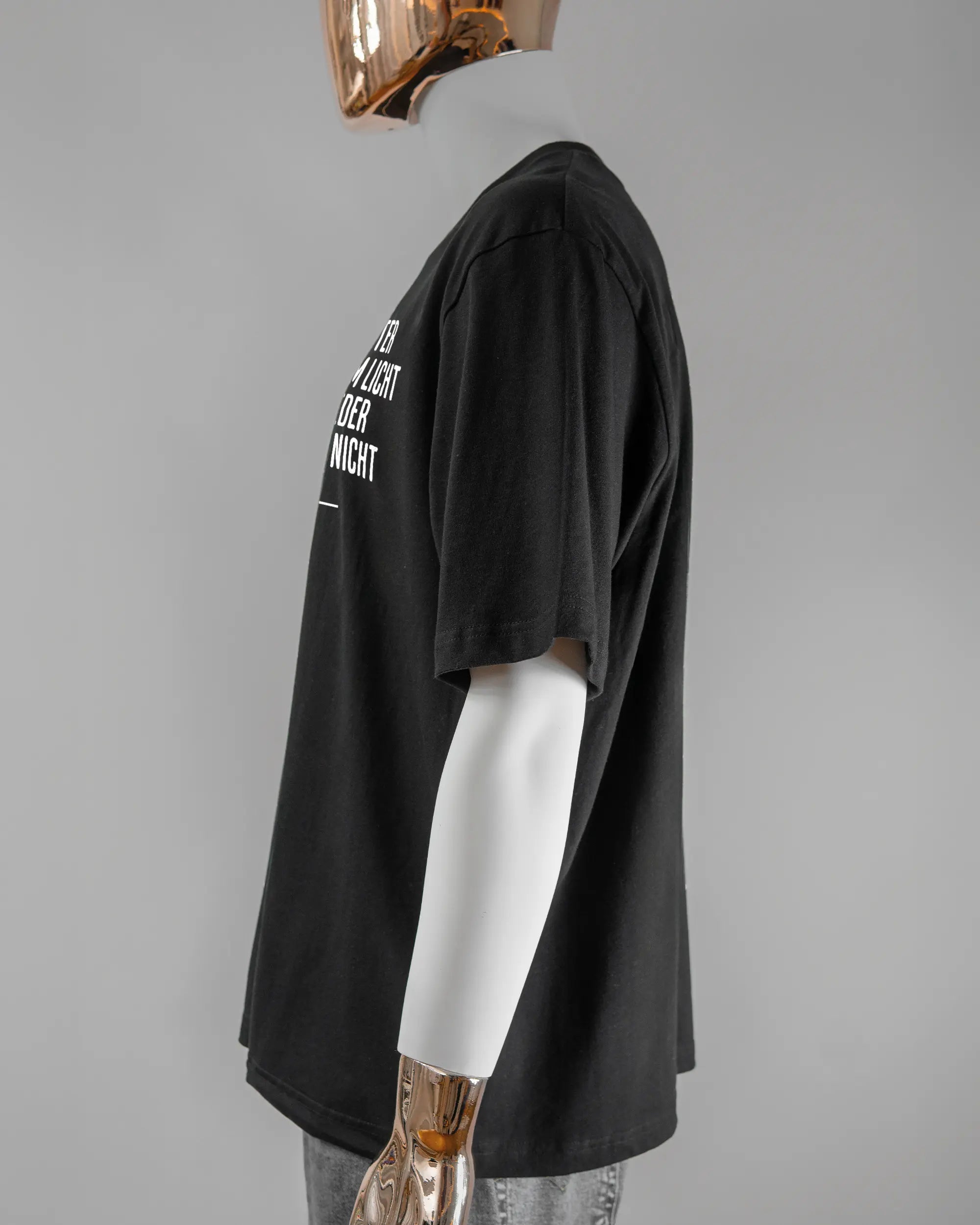 Seitenansicht des Basic Unisex T-Shirt Oversized von Maondo mit dem Design Wegzeug vorne in der Farbe Black und in der Größe L getragen von einer maskulinen Puppe