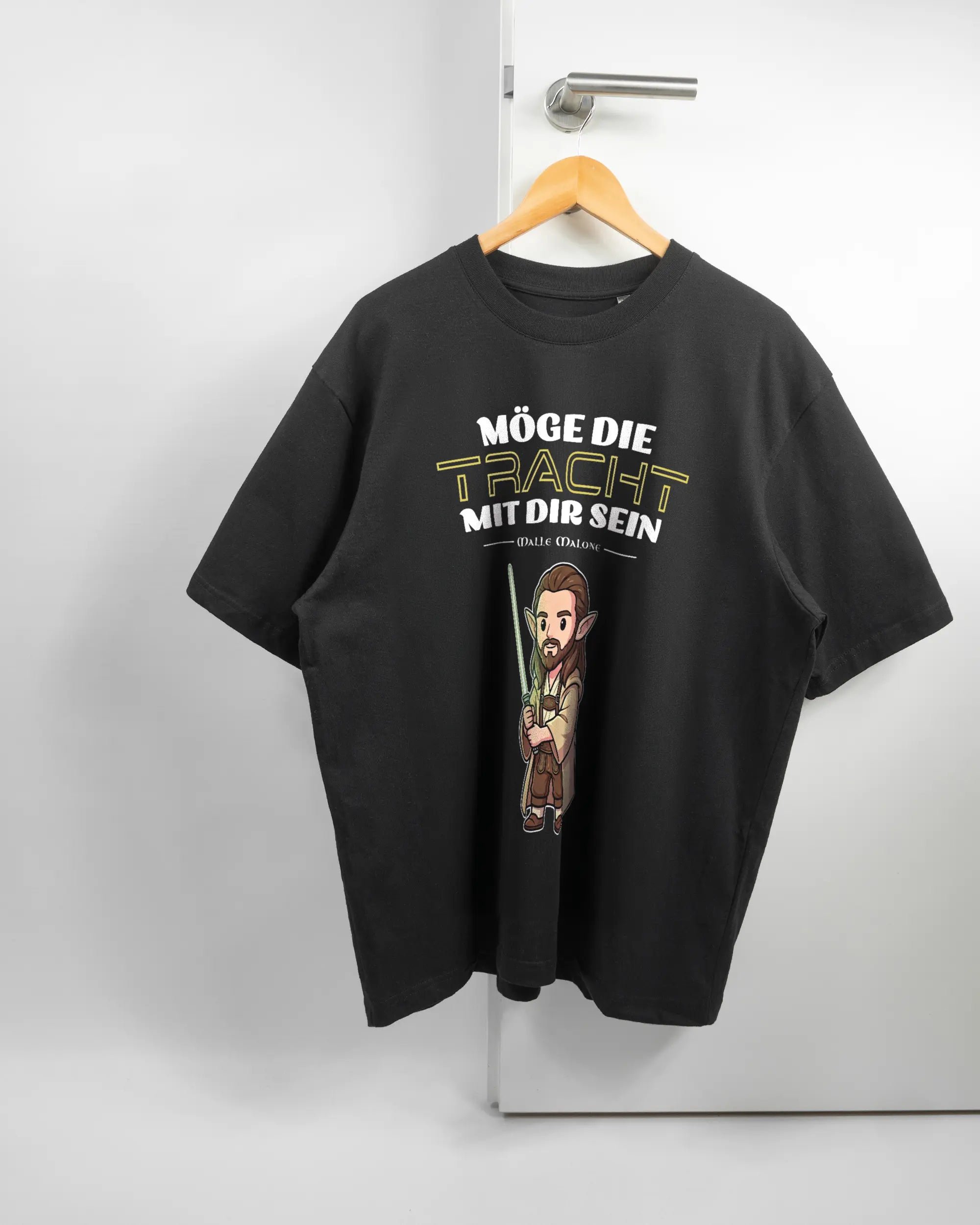 Vorderseite des Basic Unisex T-Shirt Oversized von Maondo mit dem Design Tracht mit dir in der Farbe Black und in der Größe L auf einem Bügel an der Türklinke aufgehängt