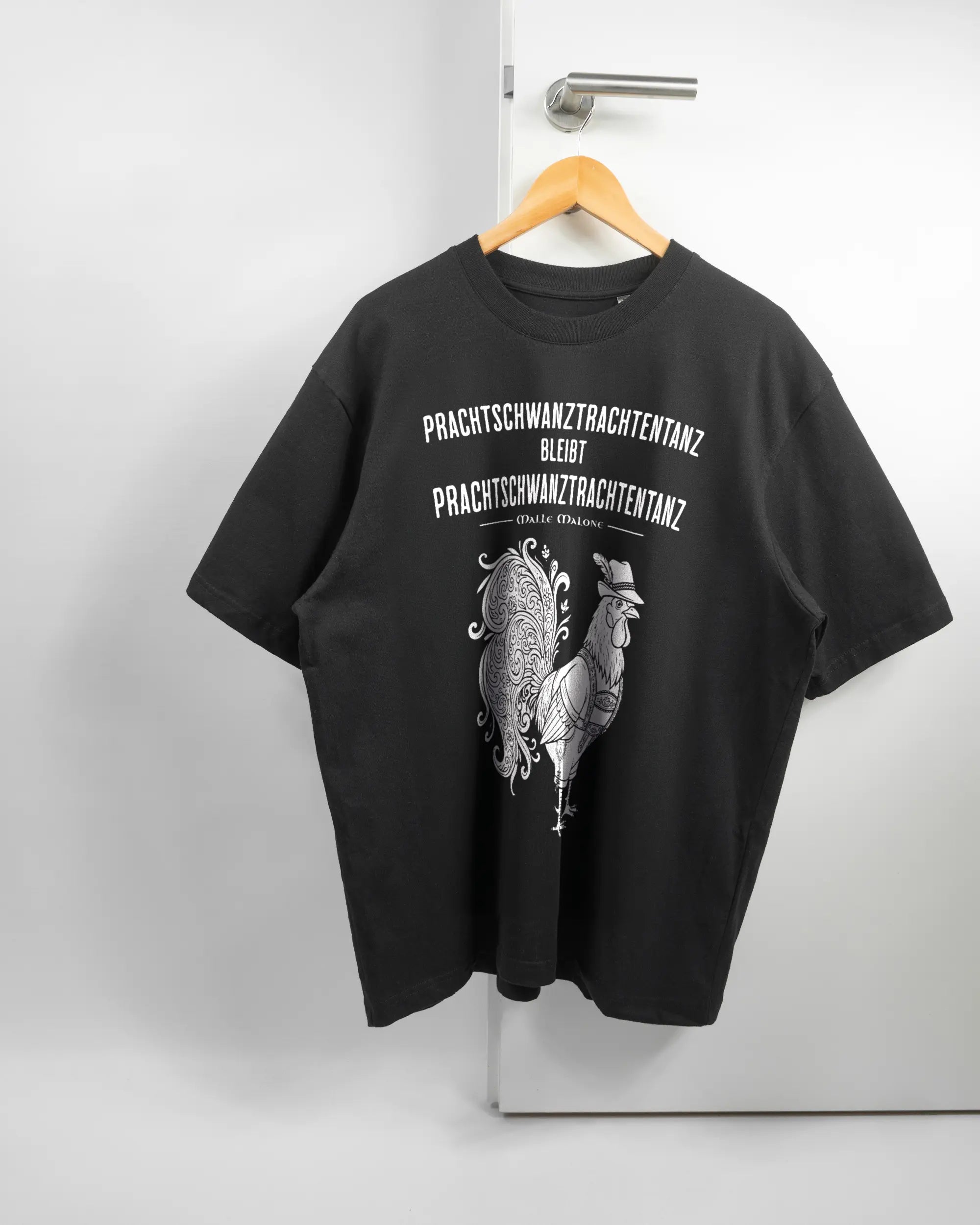 Vorderseite des Basic Unisex T-Shirt Oversized von Maondo mit dem Design Trachtentanz in der Farbe Black und in der Größe L auf einem Bügel an der Türklinke aufgehängt