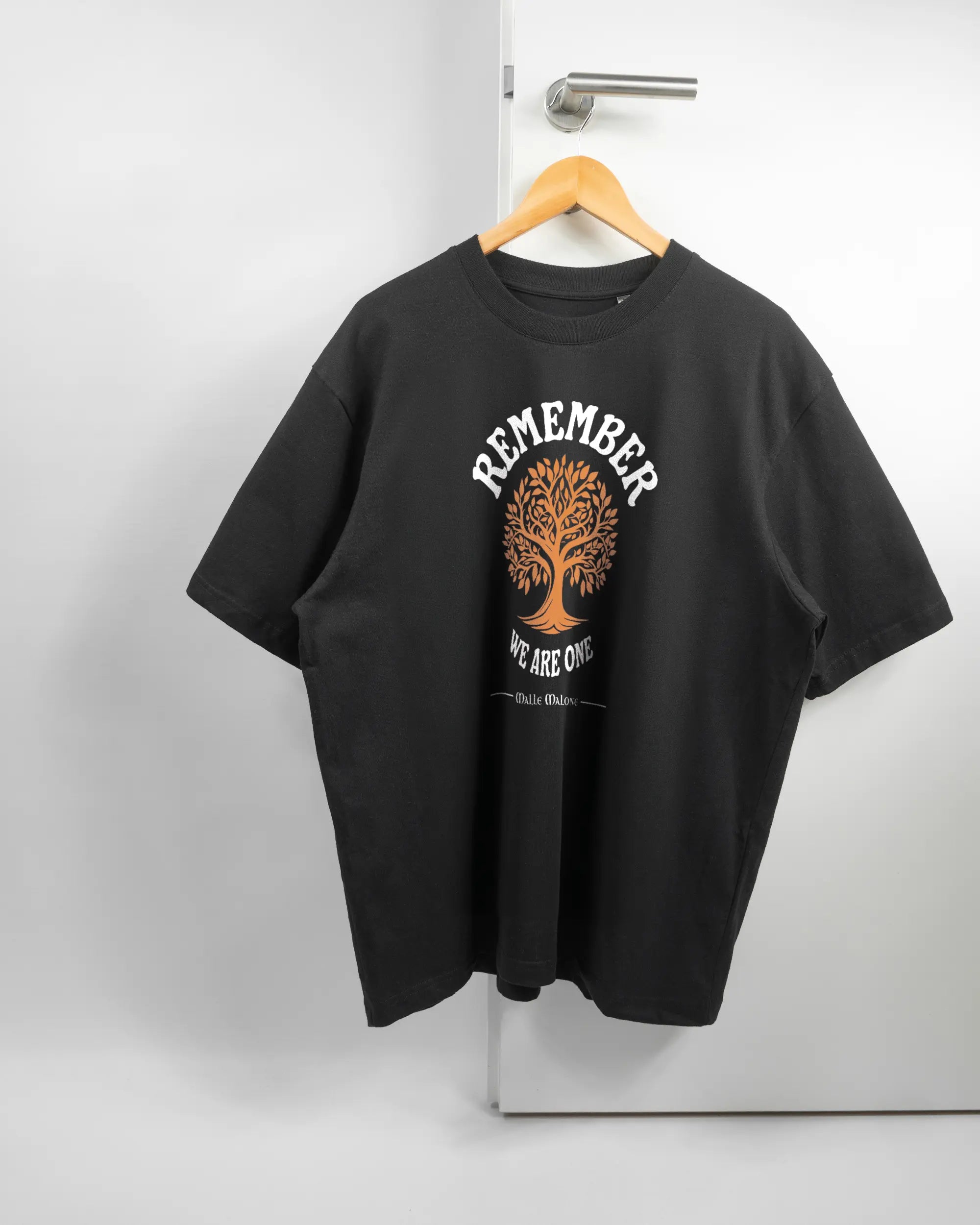 Vorderseite des Basic Unisex T-Shirt Oversized von Maondo mit dem Design We are one in der Farbe Black und in der Größe L auf einem Bügel an der Türklinke aufgehängt