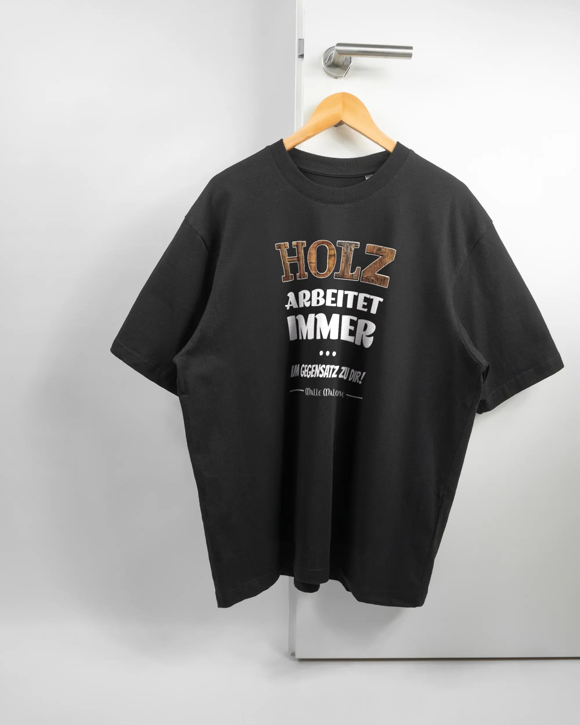 Vorderseite des Basic Unisex T-Shirt Oversized von Maondo mit dem Design Holzarbeit in der Farbe Black und in der Größe L auf einem Bügel an der Türklinke aufgehängt