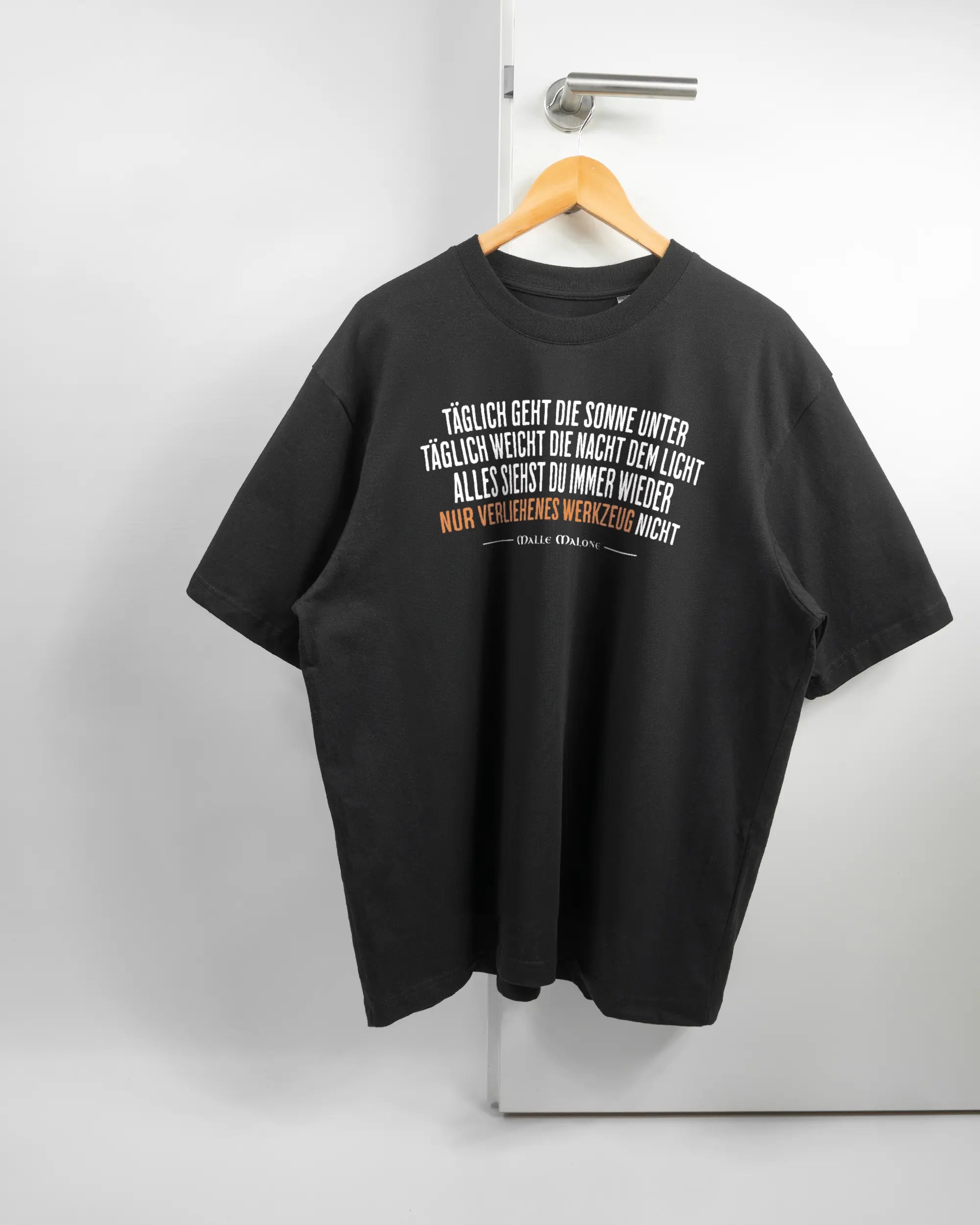 Vorderseite des Basic Unisex T-Shirt Oversized von Maondo mit dem Design Wegzeug in der Farbe Black und in der Größe L auf einem Bügel an der Türklinke aufgehängt