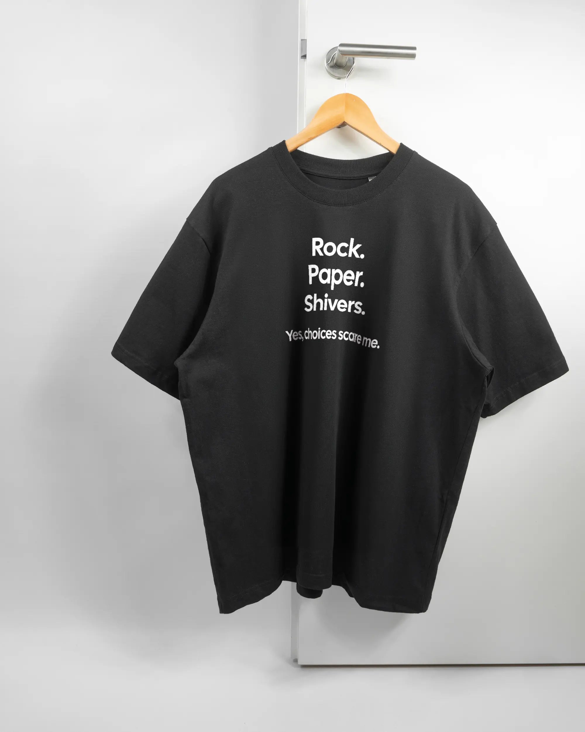 Vorderseite des Basic Unisex T-Shirt Oversized von Maondo mit dem Design Rock Paper Shivers in der Farbe Black und in der Größe L auf einem Bügel an der Türklinke aufgehängt