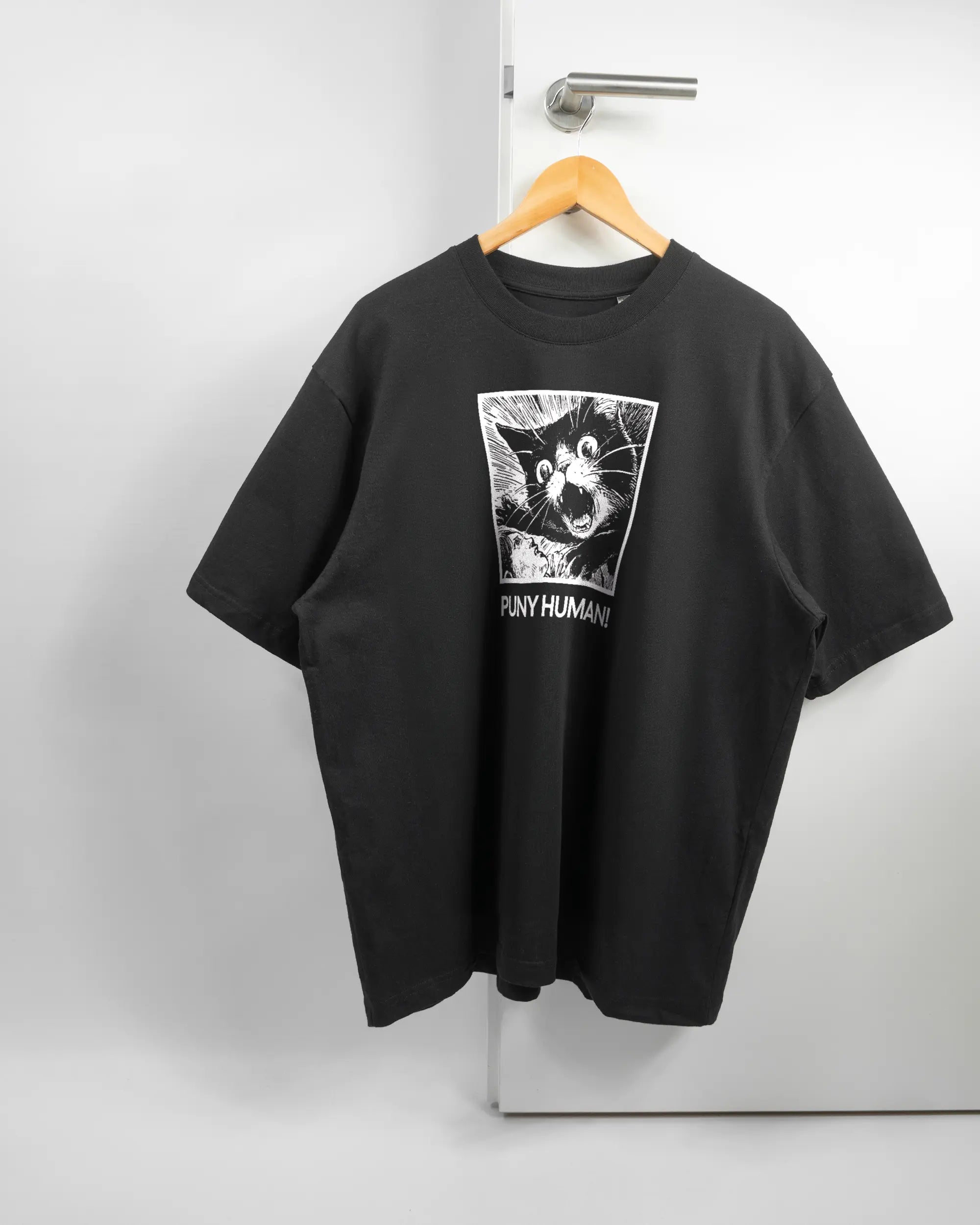 Vorderseite des Basic Unisex T-Shirt Oversized von Maondo mit dem Design Puny Human in der Farbe Black und in der Größe L auf einem Bügel an der Türklinke aufgehängt