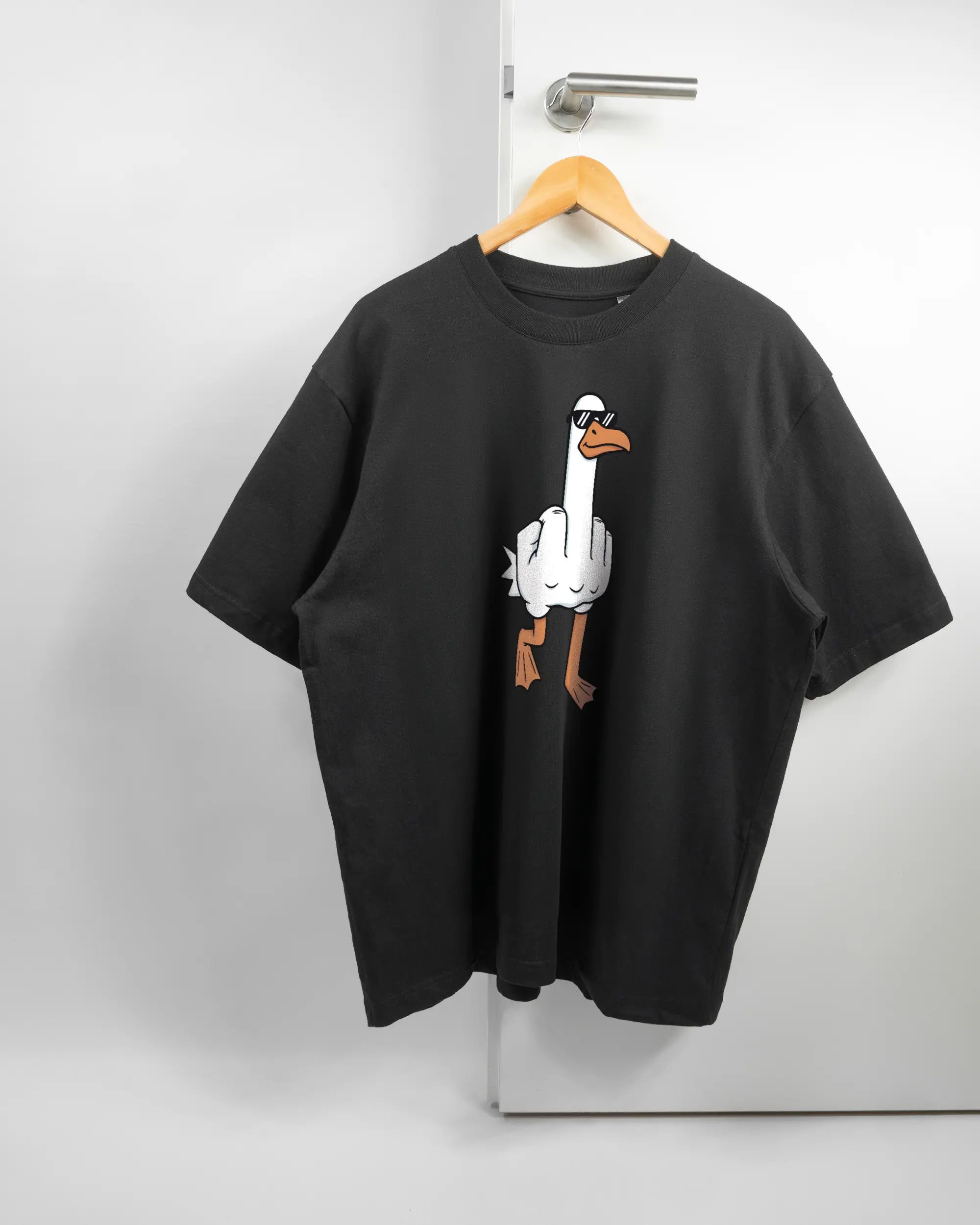 Vorderseite des Basic Unisex T-Shirt Oversized von Maondo mit dem Design I give a duck in der Farbe Black und in der Größe L auf einem Bügel an der Türklinke aufgehängt