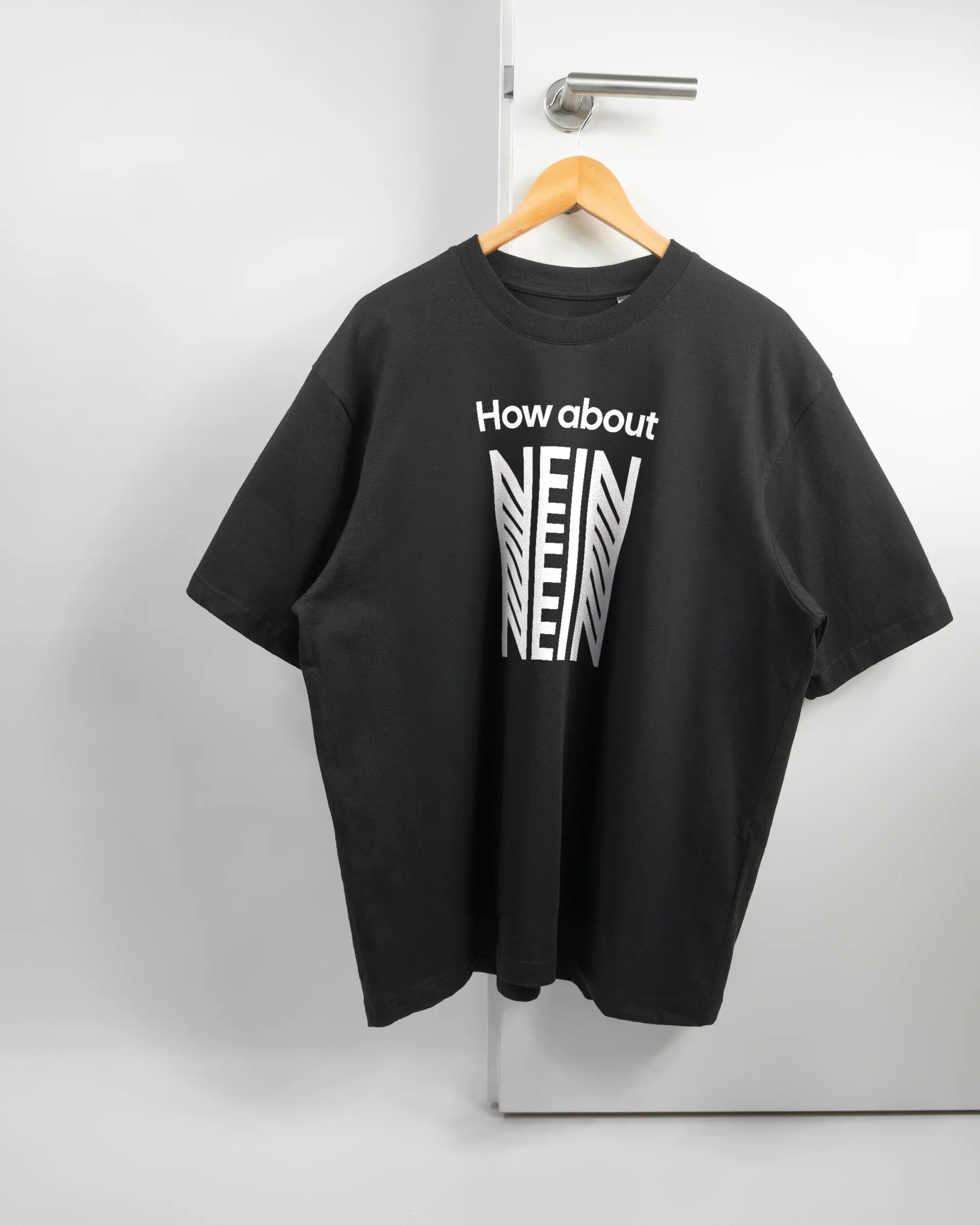 Vorderseite des Basic Unisex T-Shirt Oversized von Maondo mit dem Design How about nein in der Farbe Black und in der Größe L auf einem Bügel an der Türklinke aufgehängt