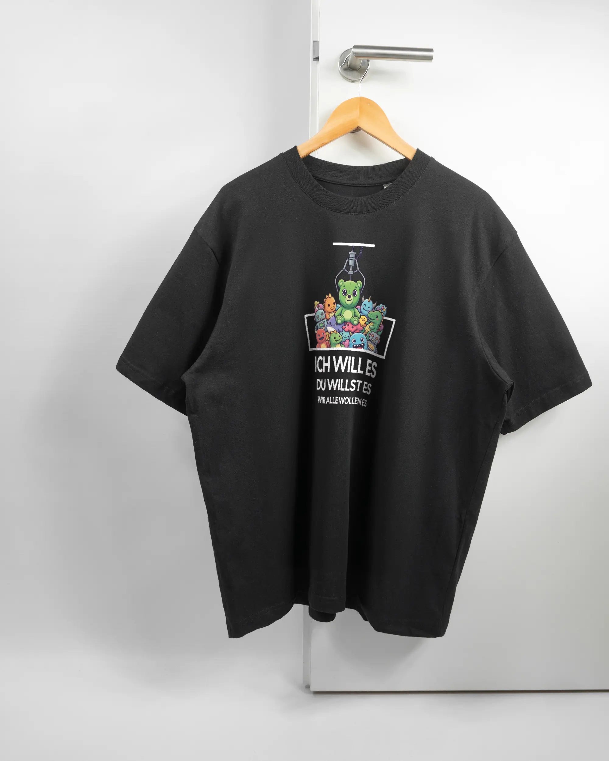 Vorderseite des Basic Unisex T-Shirt Oversized von Maondo mit dem Design Will Stofftier in der Farbe Black und in der Größe L auf einem Bügel an der Türklinke aufgehängt